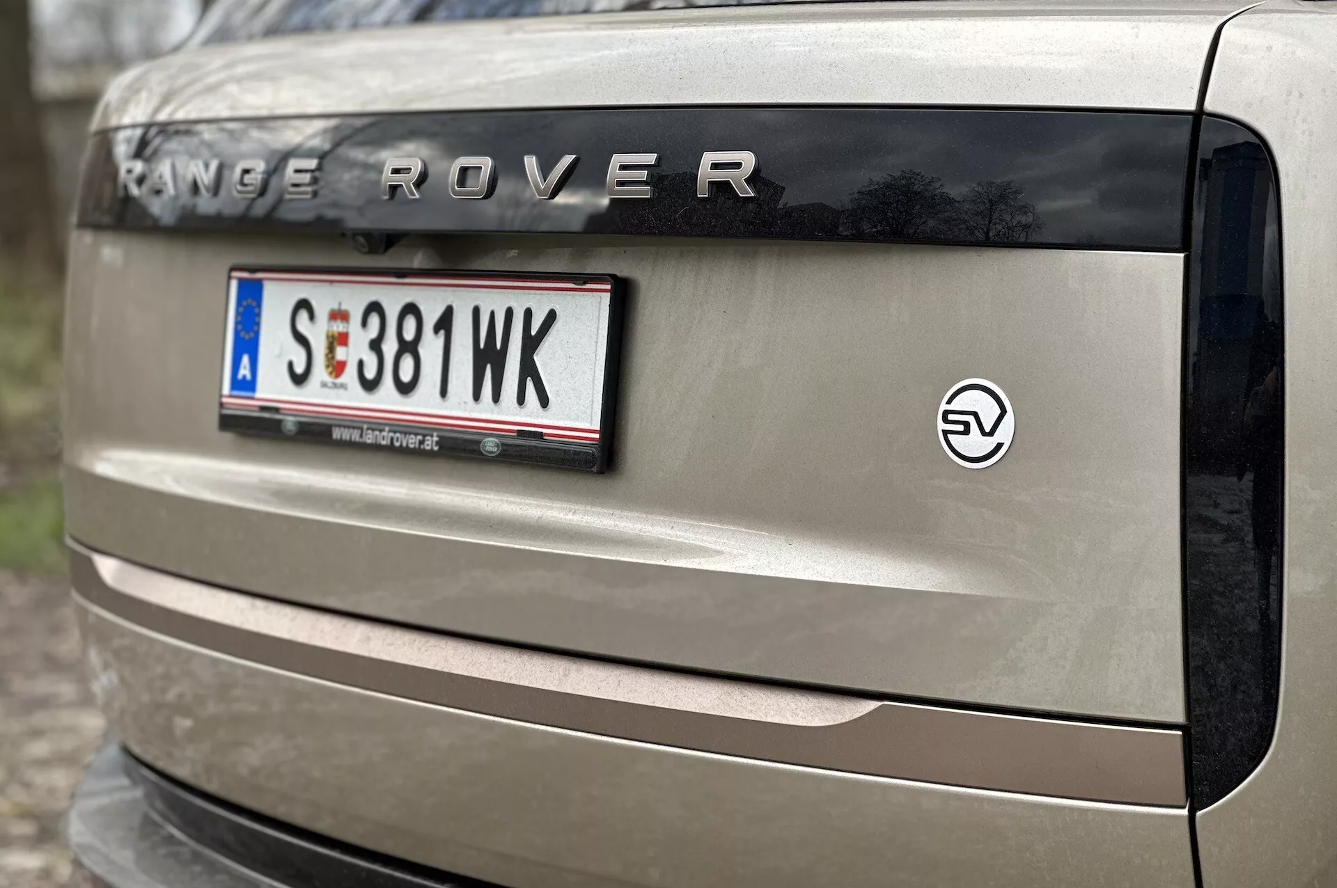 Detailný pohľad na zadnú časť vozidla Range Rover 2021 s označením 'RANGE ROVER', držiakom európskeho štýlu pre evidenčnú značku, znakom pre elektrifikáciu a časťou zadného svetla