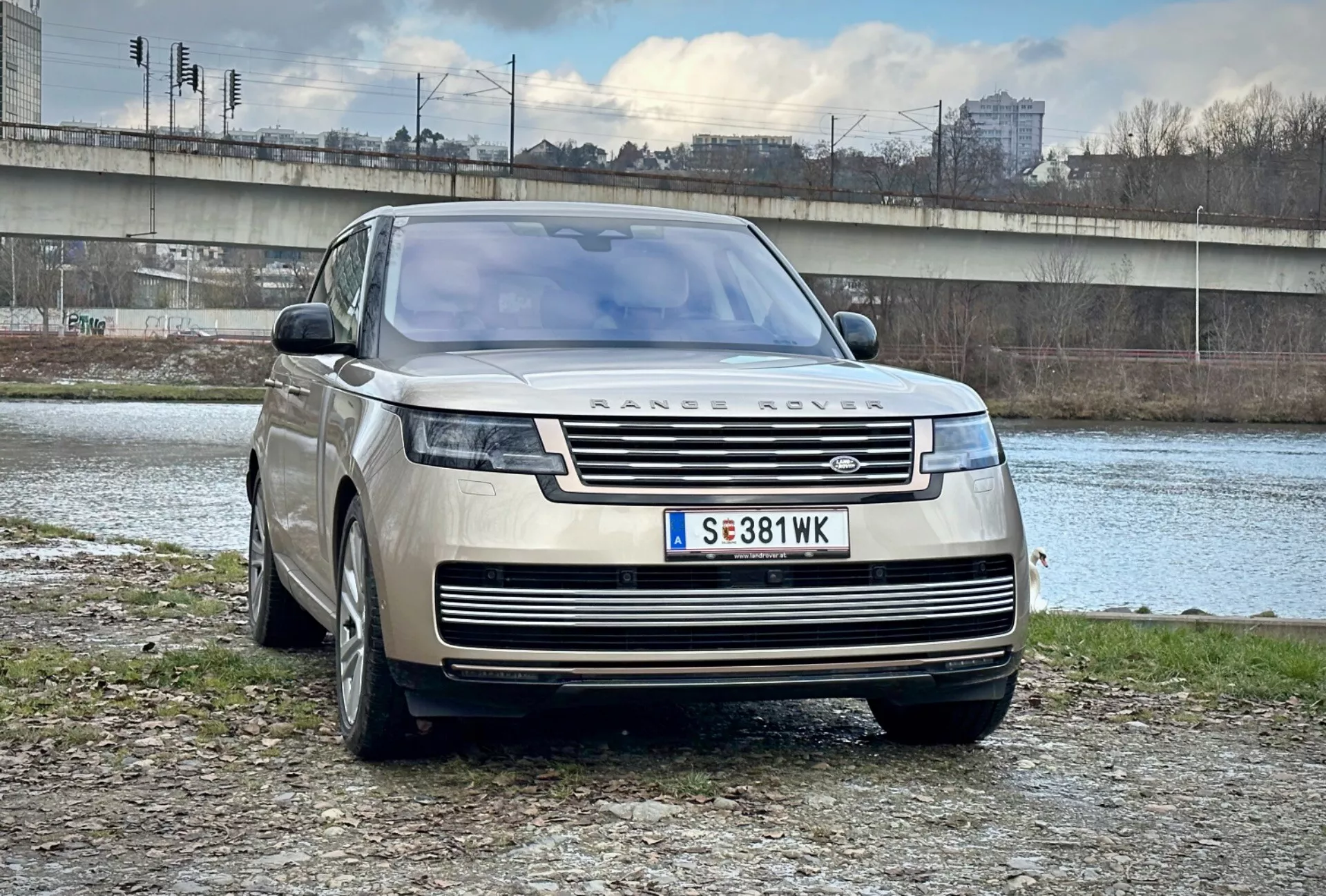 Luxusné SUV Range Rover 2021 zaparkované vonku pri rieke a moste v mestskom prostredí, predvádzajúce jeho moderný dizajn, prednú mriežku a elegantné LED svetlomety