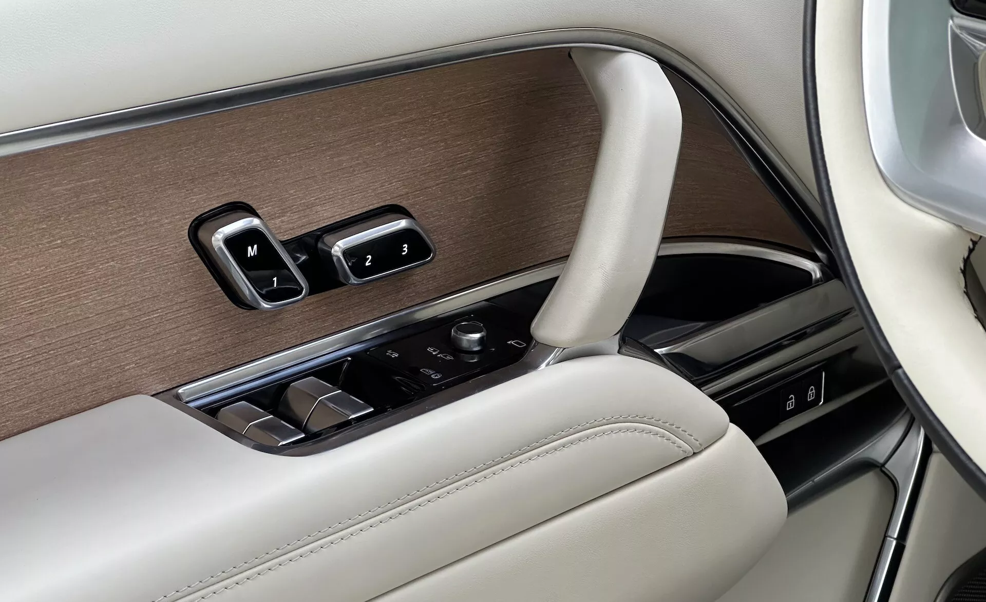 Detail interiéru Land Rover Range Rover 2021 zobrazujúci panel dverí vodiča s ovládaním okien, nastaveniami zrkadiel, nastaveniami pamäte sedadiel v luxusnom dizajne s drevodekorom, chrómom a koženým povrchom, a ovládacím gombom pre infotainment.