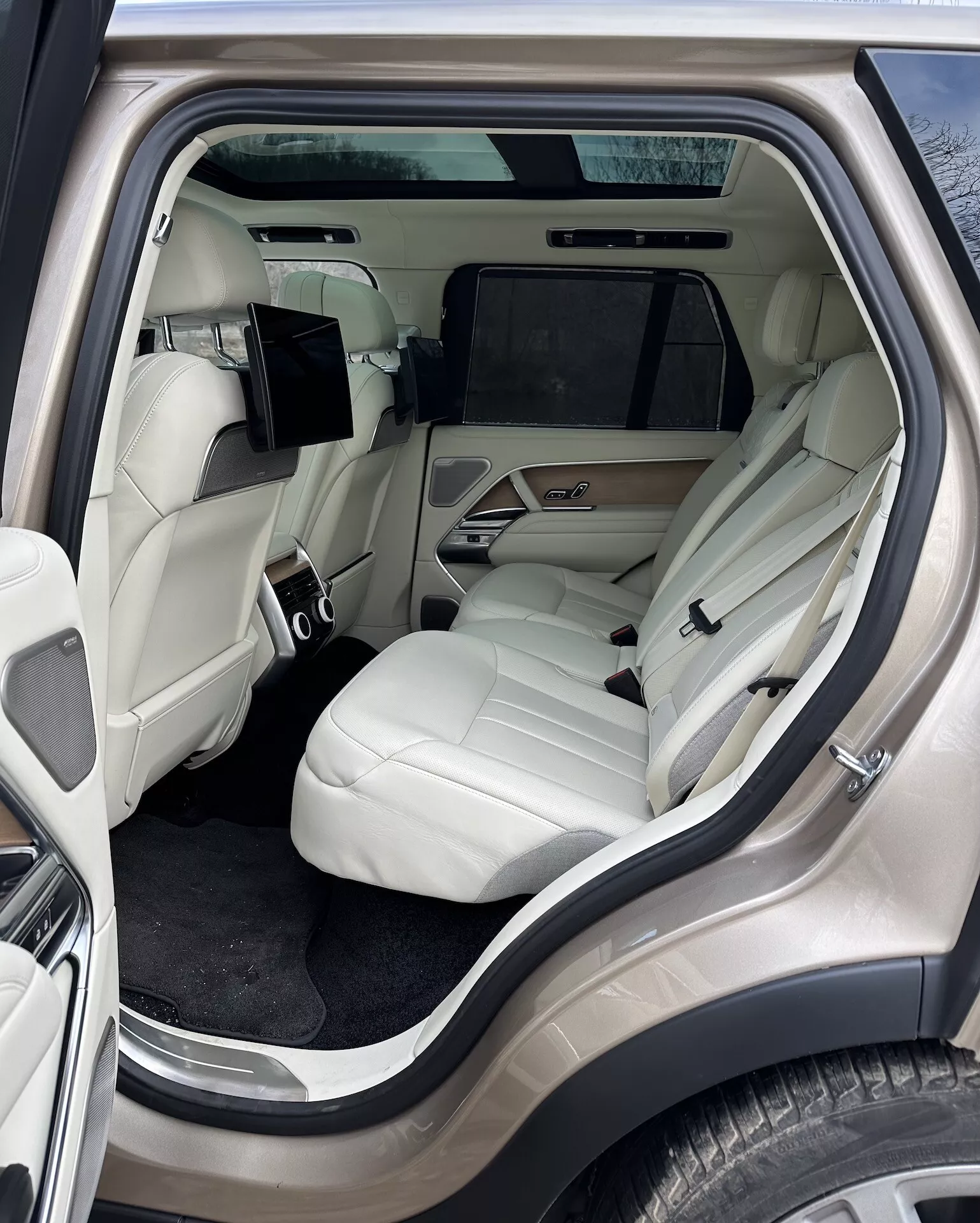Interiér Land Rover Range Rover 2021 zameraný na luxusný zadný cestovateľský priestor z vonkajšieho bočného uhla, s ​​svetlofarebnými koženými sedadlami, pokročilou stredovou konzolou, zábavným systémom a luxusnými detailmi