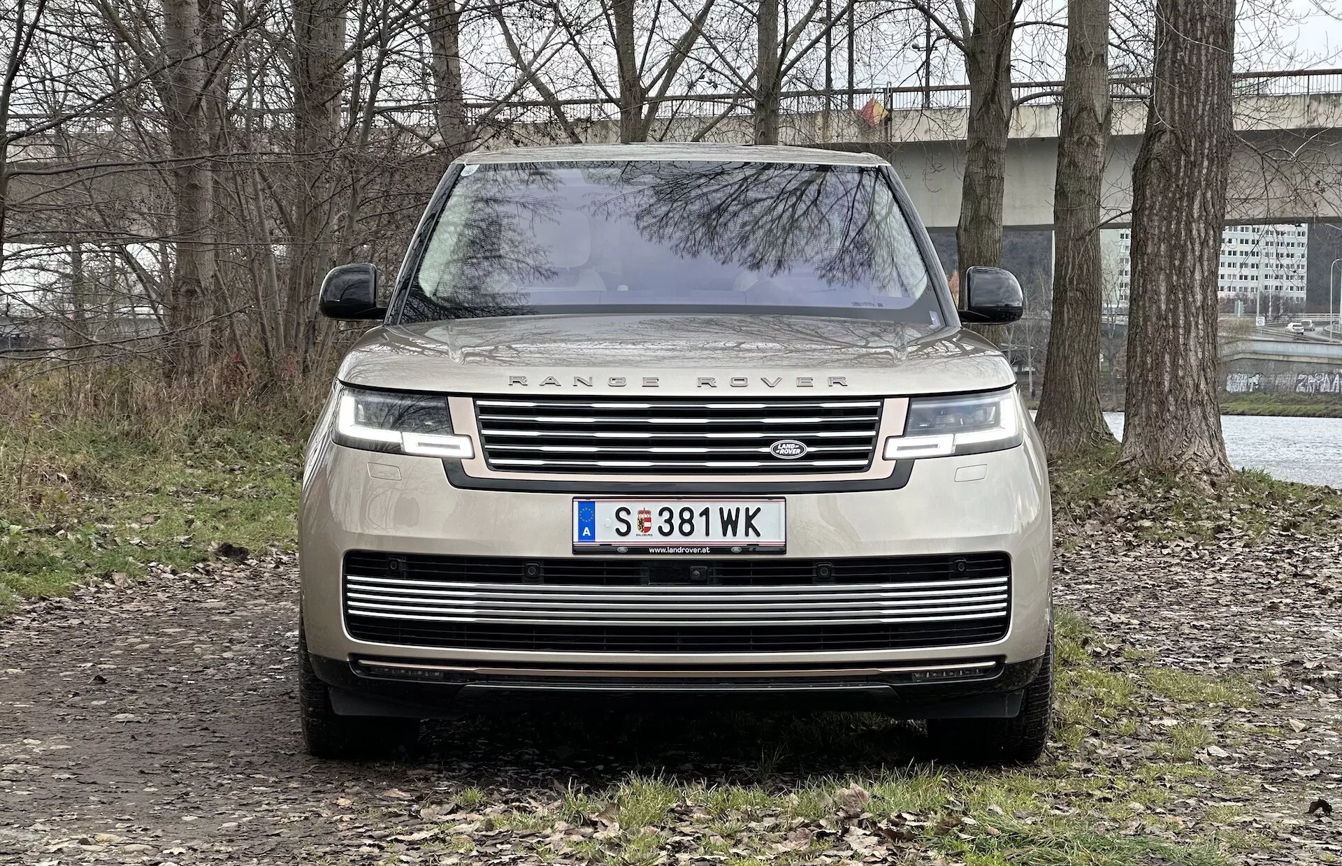 Predný pohľad na Range Rover 2021 ukazujúci mriežku, LED svetlomety, nápis 'RANGE ROVER' na kapote a zaparkovaný na neupravenej ploche so semi-vidieckym pozadím