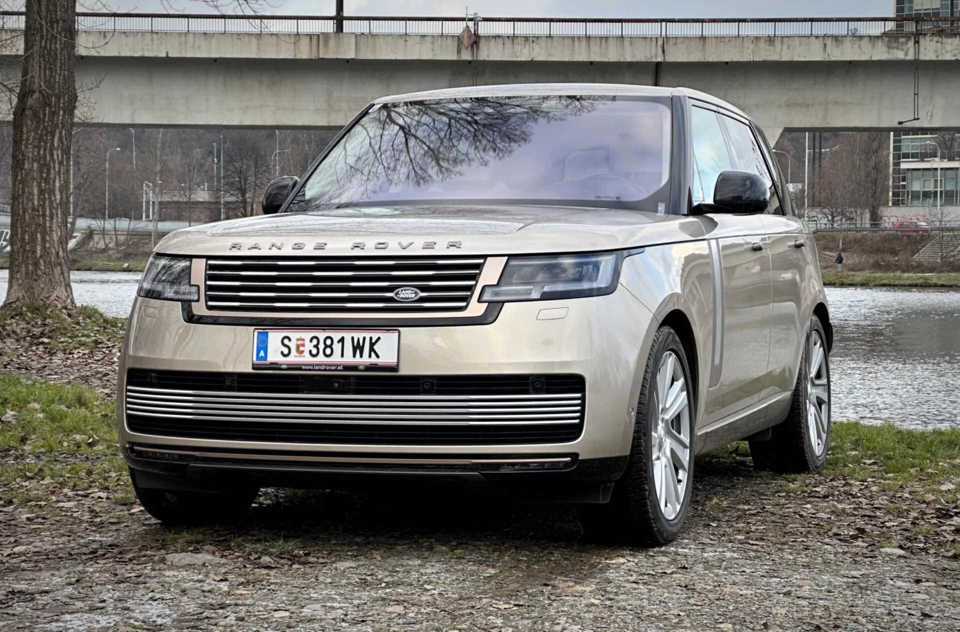 Range Rover 2021 v pôsobivom pohľade z predného trojštvrtečného uhla, ktorý zvýrazňuje jeho charakteristickú prednú mriežku, elegantné LED svetlomety a robustný predný ochranný plech proti pozadí mestského parku, čo zvýrazňuje luxus a terénnu schopnosť.