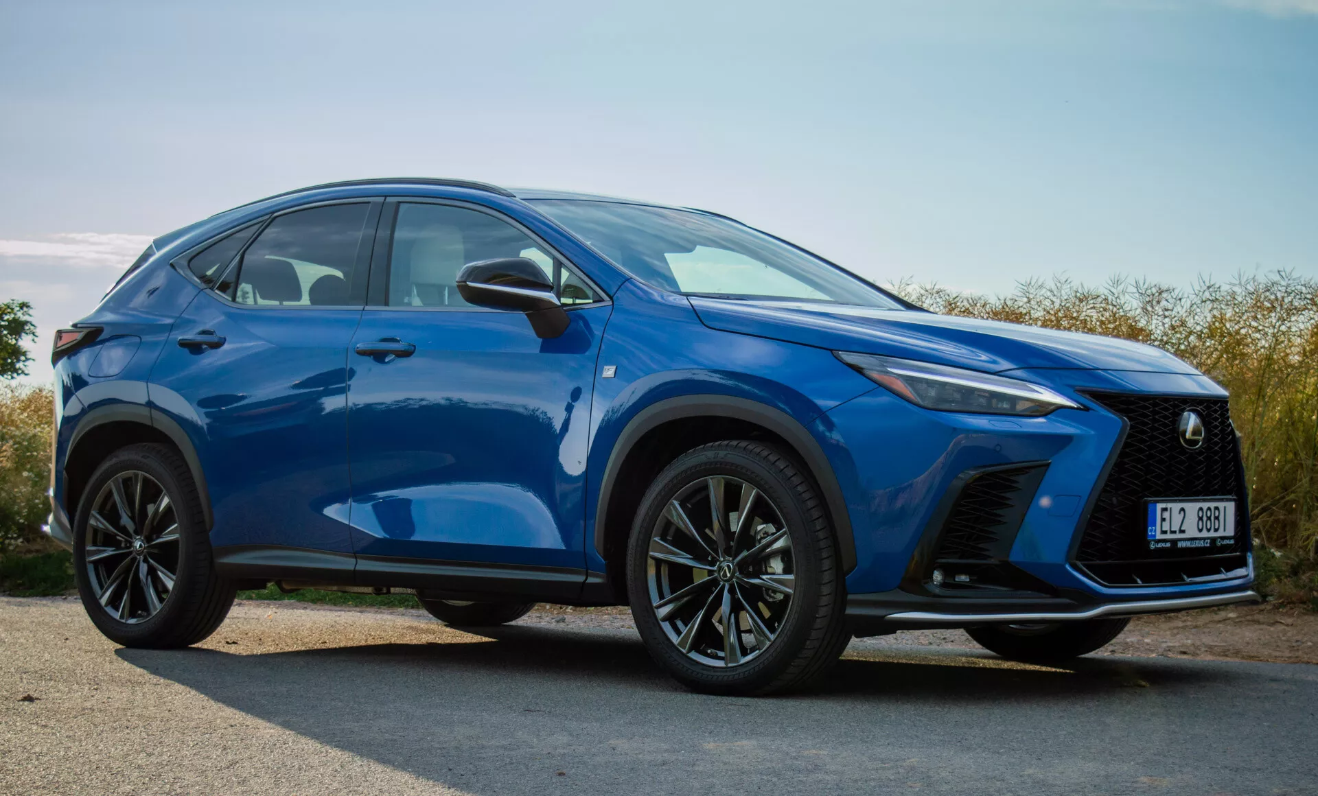 Kompaktné SUV Lexus NX 2021 vo výraznej modrej farbe predvádzajúce predný nárazník, mriežku, LED svetlomety, kapotu, kolesá a línie bočných kontúr z pohľadu z troch štvrtín spredu vonku vo dne