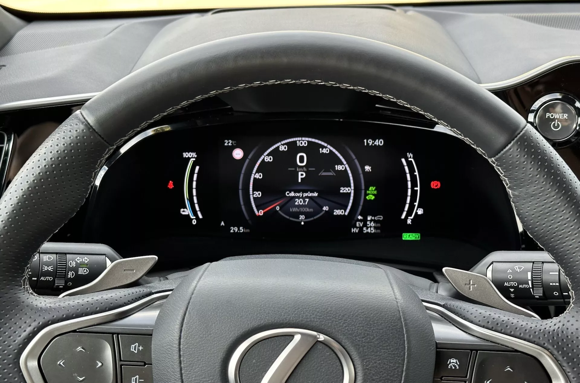 Pohľad z miesta vodiča na volant a digitálny prístrojový panel Lexus NX 2021, zdôraznenie indikátorov hybridnej technológie, tlačidiel pre ovládanie komfortu a ergonomického dizajnu interiéru