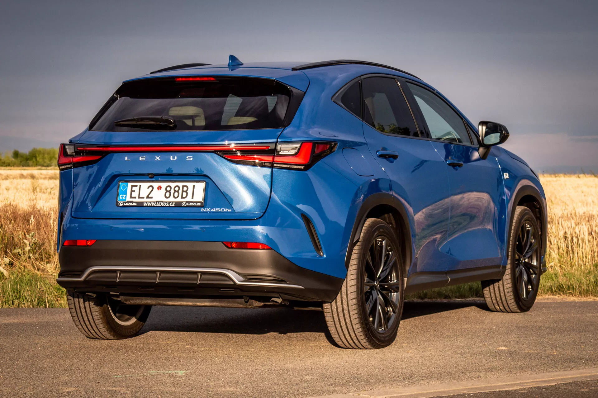 Modré SUV Lexus NX 2021 v zobrazení zo zadného trojštvrtečného uhla, ktoré prezentuje dizajnové prvky a technologické funkcie na slnečný deň s prírodným pozadím