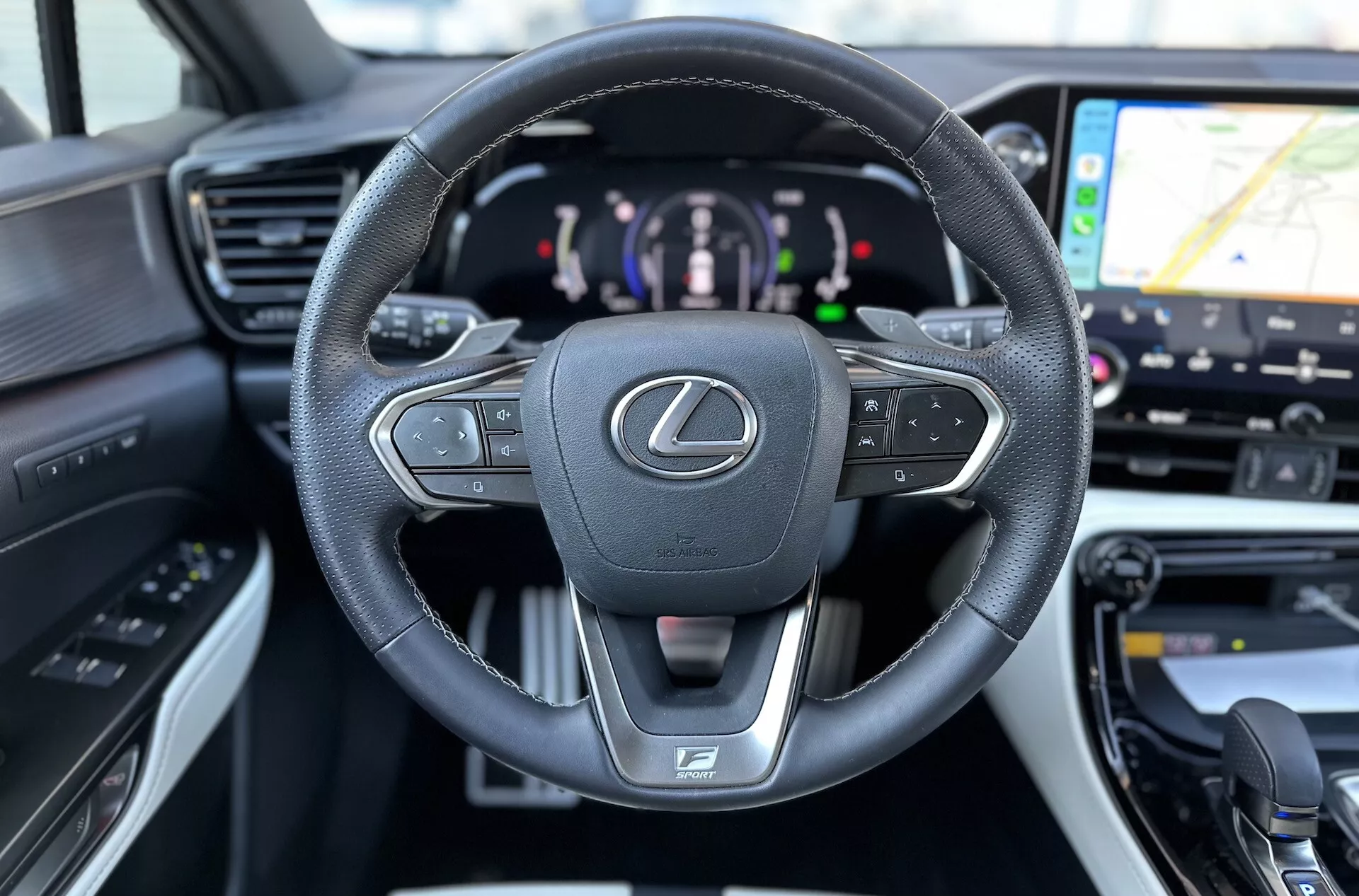 Interiér Lexus NX 2021 s dôrazom na kožou potiahnutý, multifunkčný volant s emblémom Lexus a logom F SPORT, digitálny prístrojový panel naznačujúci hybridný pohon a náhľad na GPS navigáciu na systéme infotainmentu