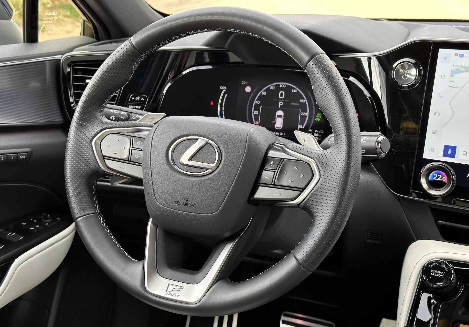 Interiérový pohľad na Lexus NX 2021 so zameraním na volant a palubnú dosku, zobrazujúci multifunkčné tlačidlá, digitálny prístrojový panel, dotykovú obrazovku infotainmentu, kožené akcenty, volič režimu jazdy, ventilačné otvory a detailné šitie.