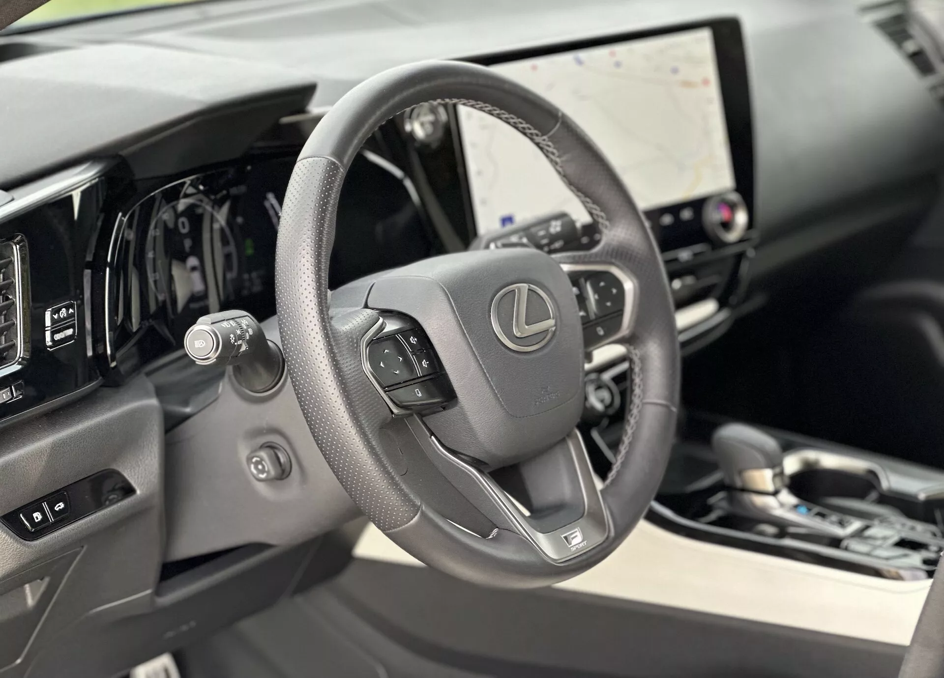 Pohľad do interiéru Lexusu NX 2021 s dôrazom na kožený volant s ovládacími prvkami a digitálny palubný panel za ním, predstavujúci veľkú dotykovú obrazovku infotainmentu a jemné náznaky luxusu vo vysokokvalitných materiáloch