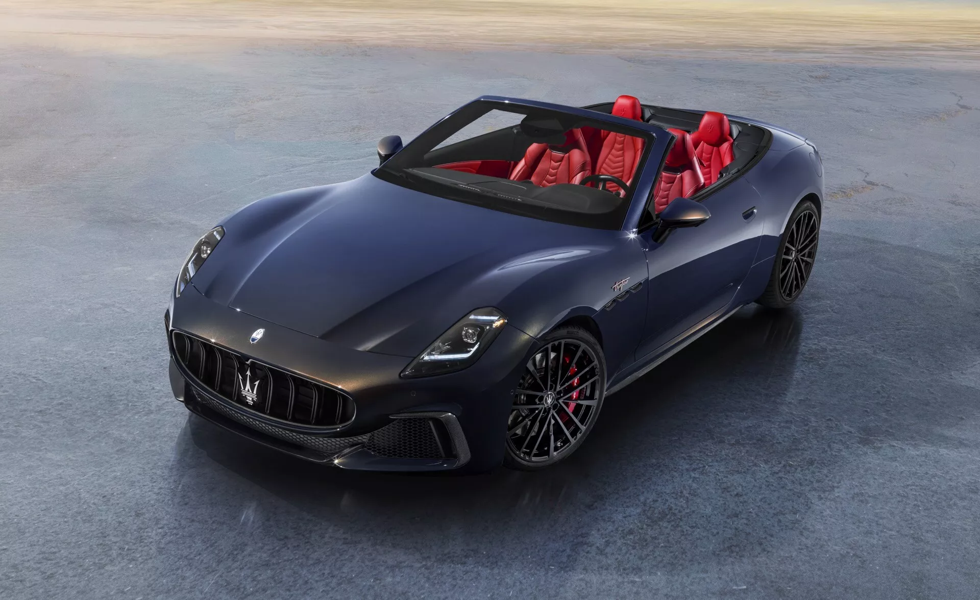Maserati GranCabrio 2. generácia 2024 v metalickej tmavomodrej alebo sivej farbe s LED svetlometmi, zliatinovými kolesami s viacerými lúčmi, červeným interiérom a vysokým leskom, zachytené z vtáčej perspektívy zdôrazňujúce luxusné a výkonnostné vlastnosti auta.