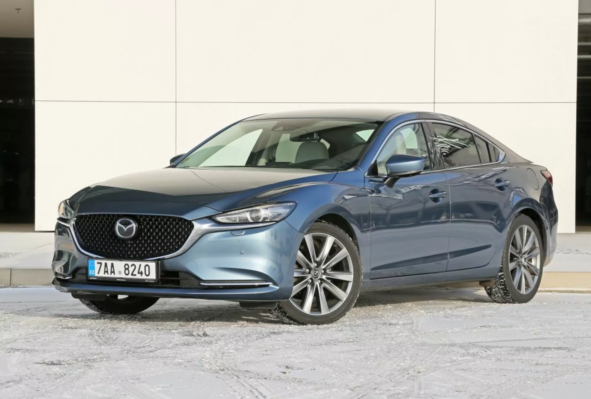 Modrý sedan Mazda 6 z roku 2013, ukazuje pohľad z trojštvrtečného predného uhla na čelnú mriežku, emblém, štýlové predné svetlomety a zliatinové kolesá na zimnom asfalte