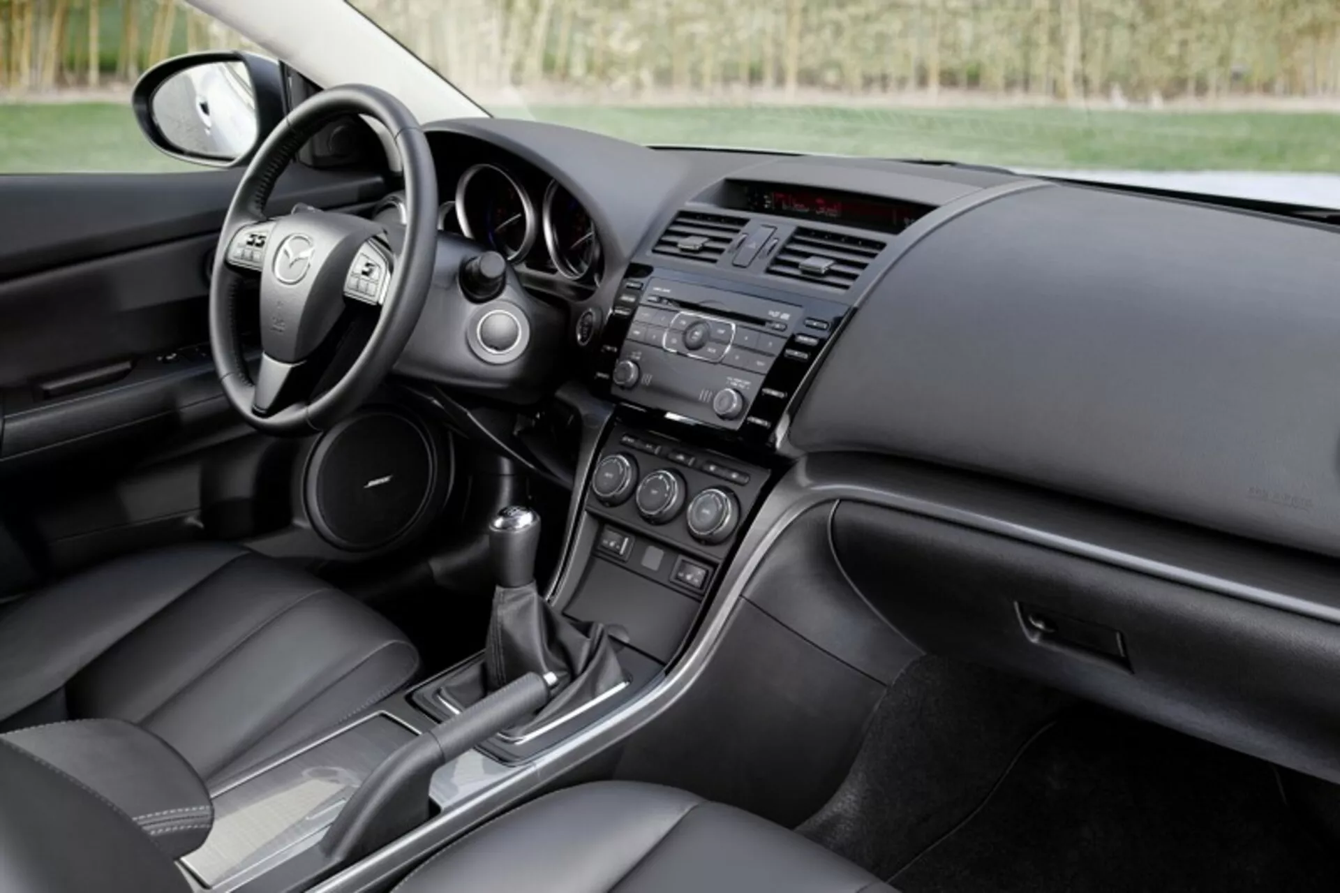 Interiér sedanu Mazda 6 z roku 2008 zobrazuje kokpit vodiča a pohľad na palubnú dosku spolujazdca s ovládacími prvkami na volante, systémami infotainmentu a klimatizácie a konzolou automatickej prevodovky, čo zdôrazňuje moderný dizajn a technologické prvky automobilu.