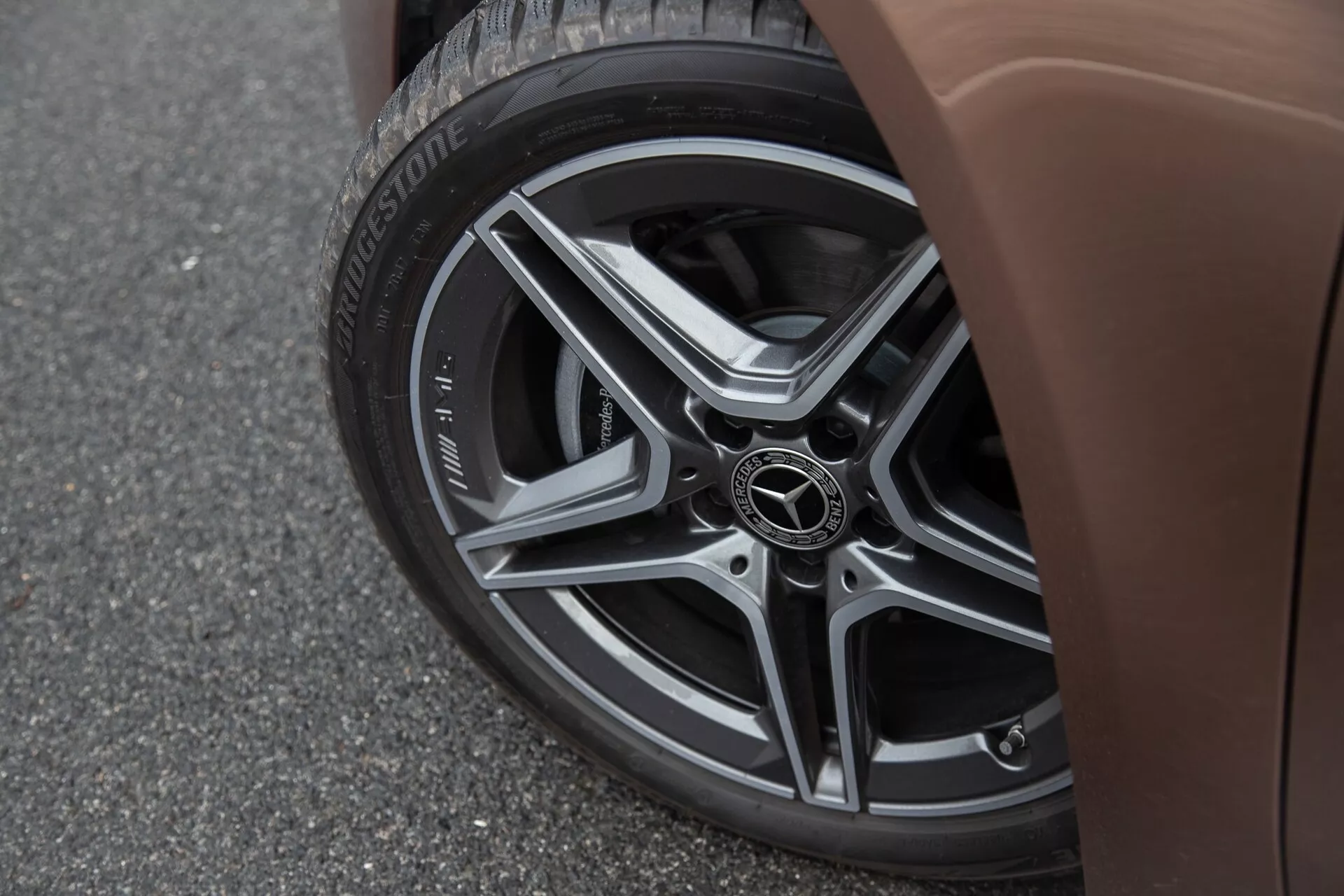 Detailný pohľad na dolnú bočnú časť Mercedesu-Benz A-Klasse 2022 s viaceročným zliatinovým kolesom, pneumatikou Bridgestone Turanza a hnedým bočným panelom na asfaltovom pozadí