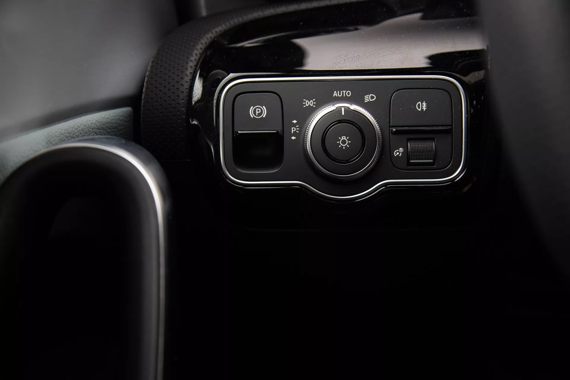 Detailný pohľad na ovládací panel svetlometov Mercedes-Benz triedy A z roku 2022 na prístrojovej doske, s tlačidlami pre parkovacie svetlo, automatický systém a hmlové svetlá alebo systém vyrovnávania svetlometov a otočným regulátorom pre nastavenie svetiel, uzavretý v lesklom čiernom rámiku.