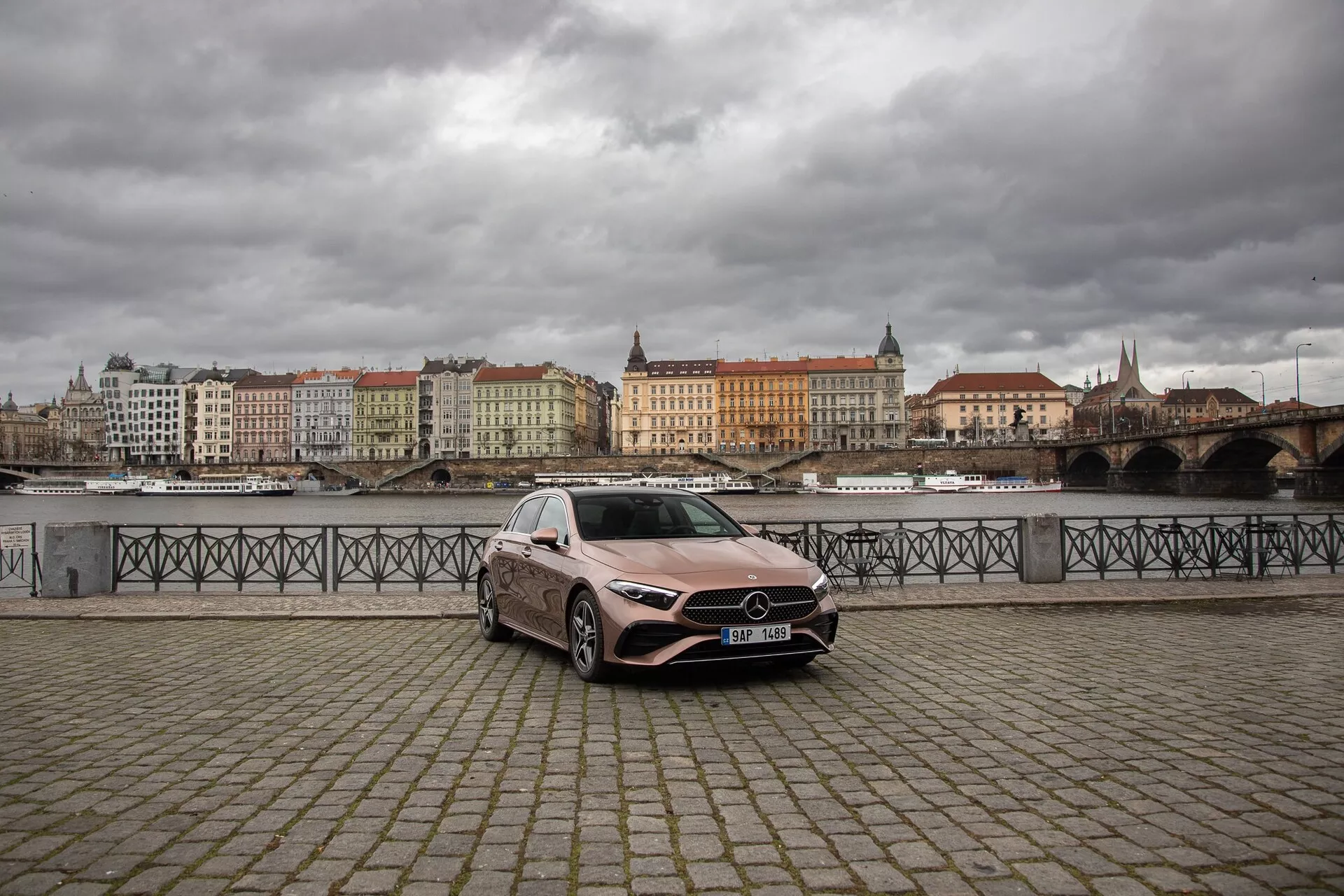 Mercedes-Benz triedy A z roku 2022 zaparkovaný na nábrežnej promenáde s povrchom z dlažobných kameňov, ukazujúci jeho predný ľavý štvrťrok s výraznou mriežkou, LED svetlometmi a veľkými zliatinovými kolesami proti pozadiu európskeho mesta