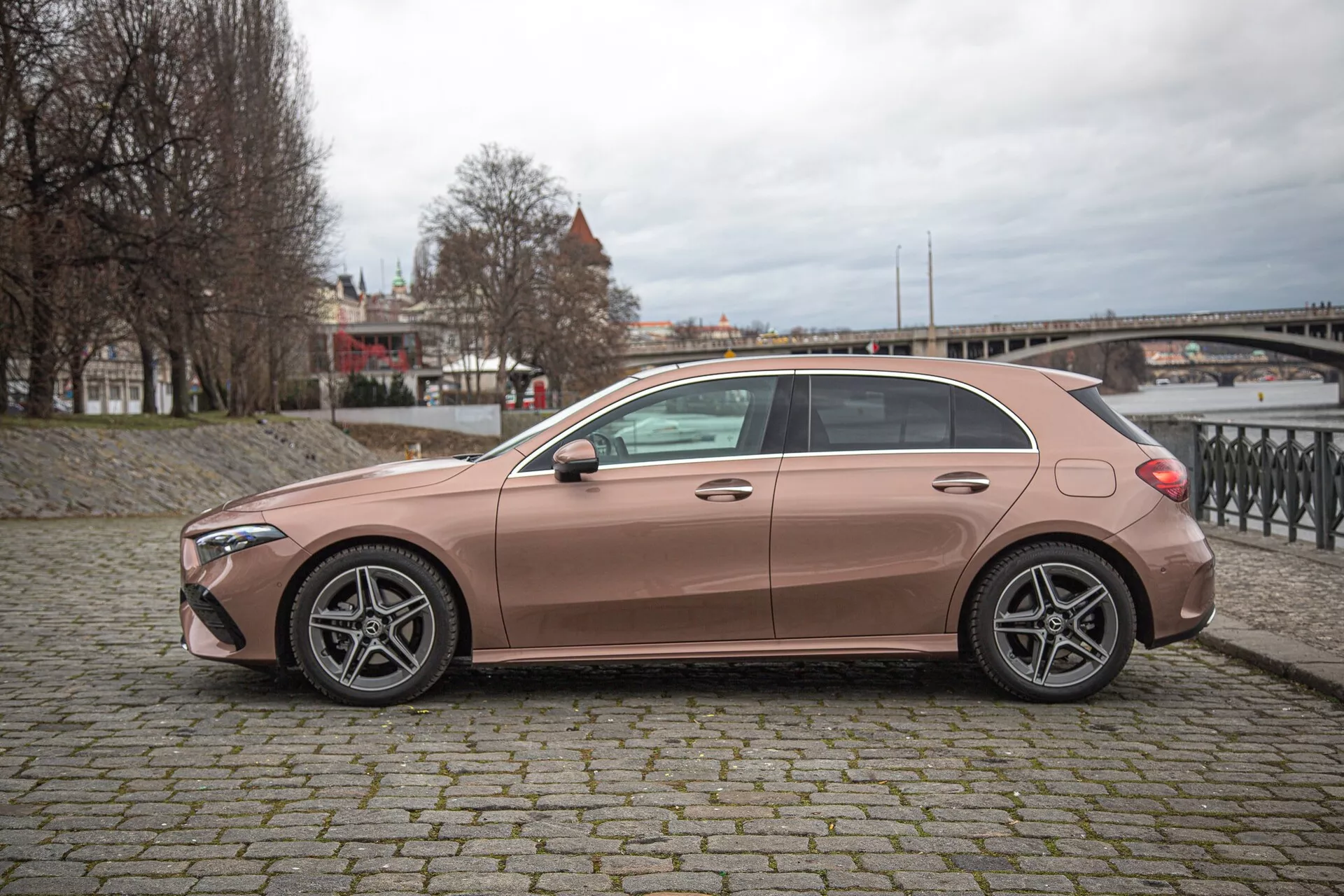 Bočný profil hatchbacku Mercedes-Benz A-Class 2022 v metalickej medi, s päťramennými zliatinovými kolesami, bezkľúčovým prístupom a aerodynamickým dizajnom v mestskom prostredí