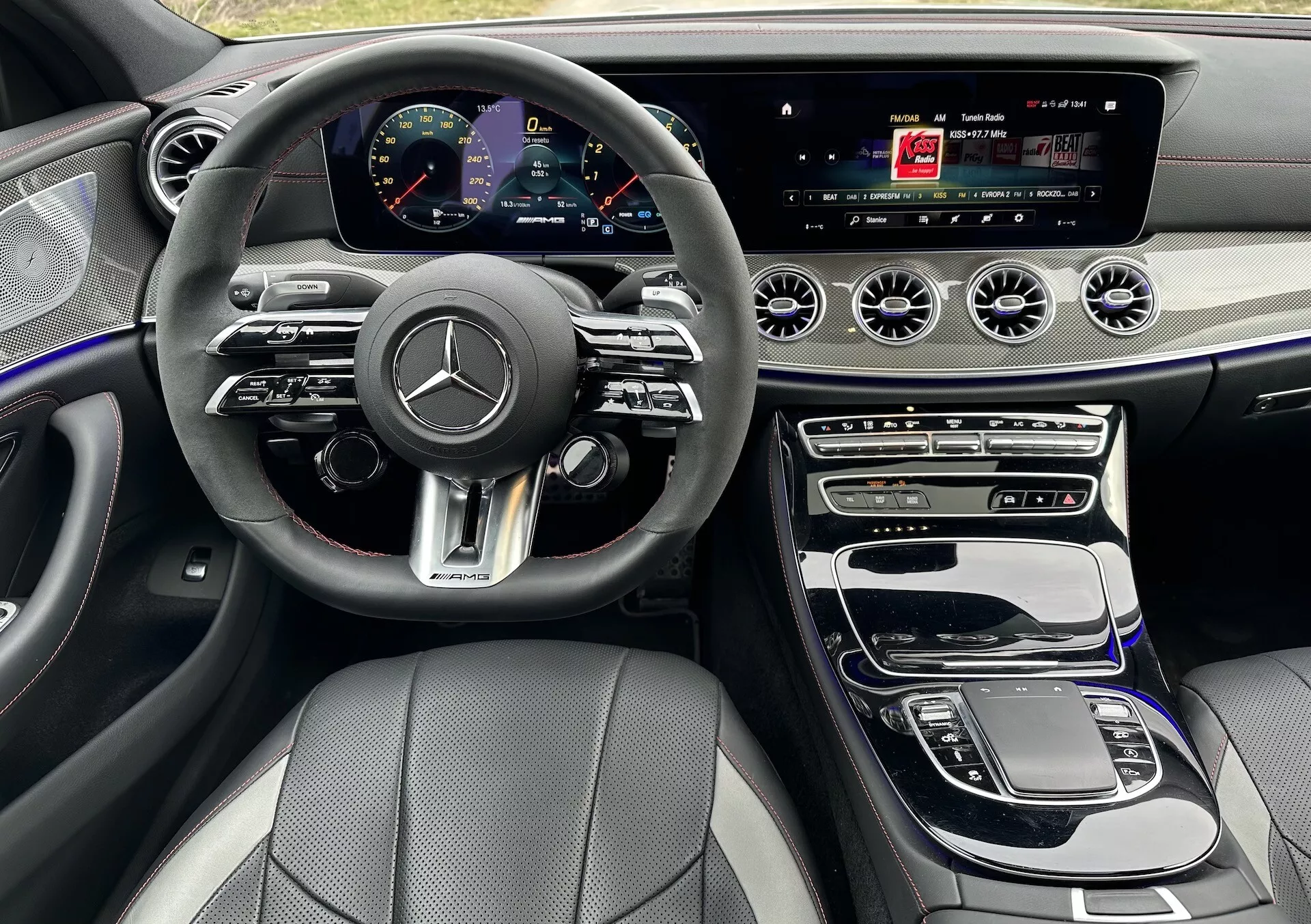 Interiér Mercedes-Benz CLS AMG Coupe 2021 s multifunkčným volantom potiahnutým kožou s chrómovými doplnkami, digitálnym prístrojovým panelom, širokoúhlym informačným displejom, dotykovou centrálnou konzolou obklopenou drevotrieskovým obkladom, duálnou klimatizáciou a prémiovými čiernymi kožennými sedadlami so vzorovaným šitím.