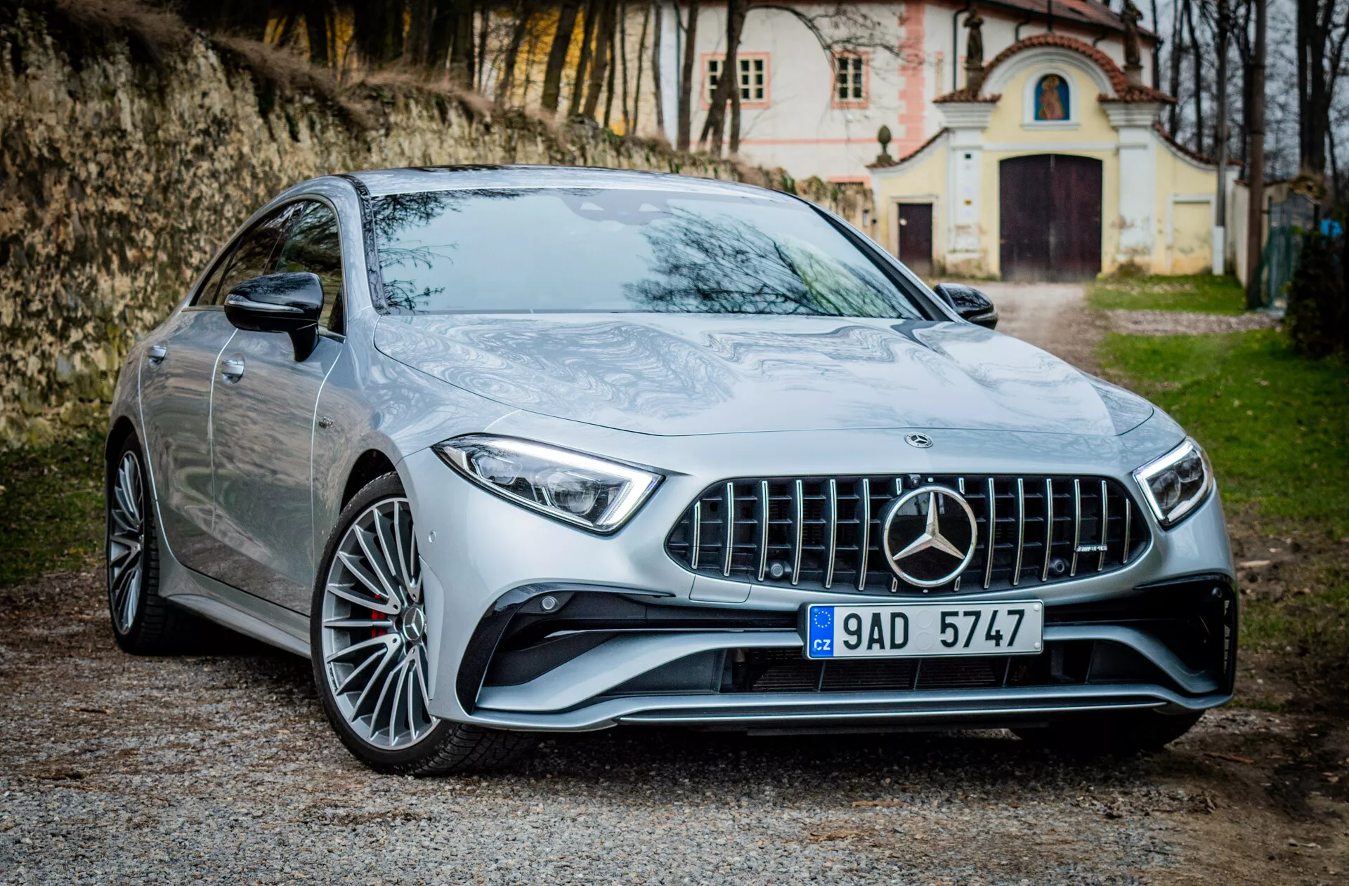 Strieborné kupé Mercedes-Benz CLS AMG 2021, parkované vonku, predvádzajúce svoj uhlový predný dizajn s LED svetlometmi, športovou mriežkou AMG s textúrou diamantového bloku a senzormi pokročilých asistenčných systémov vodiča integrovanými do predného nárazníka.
