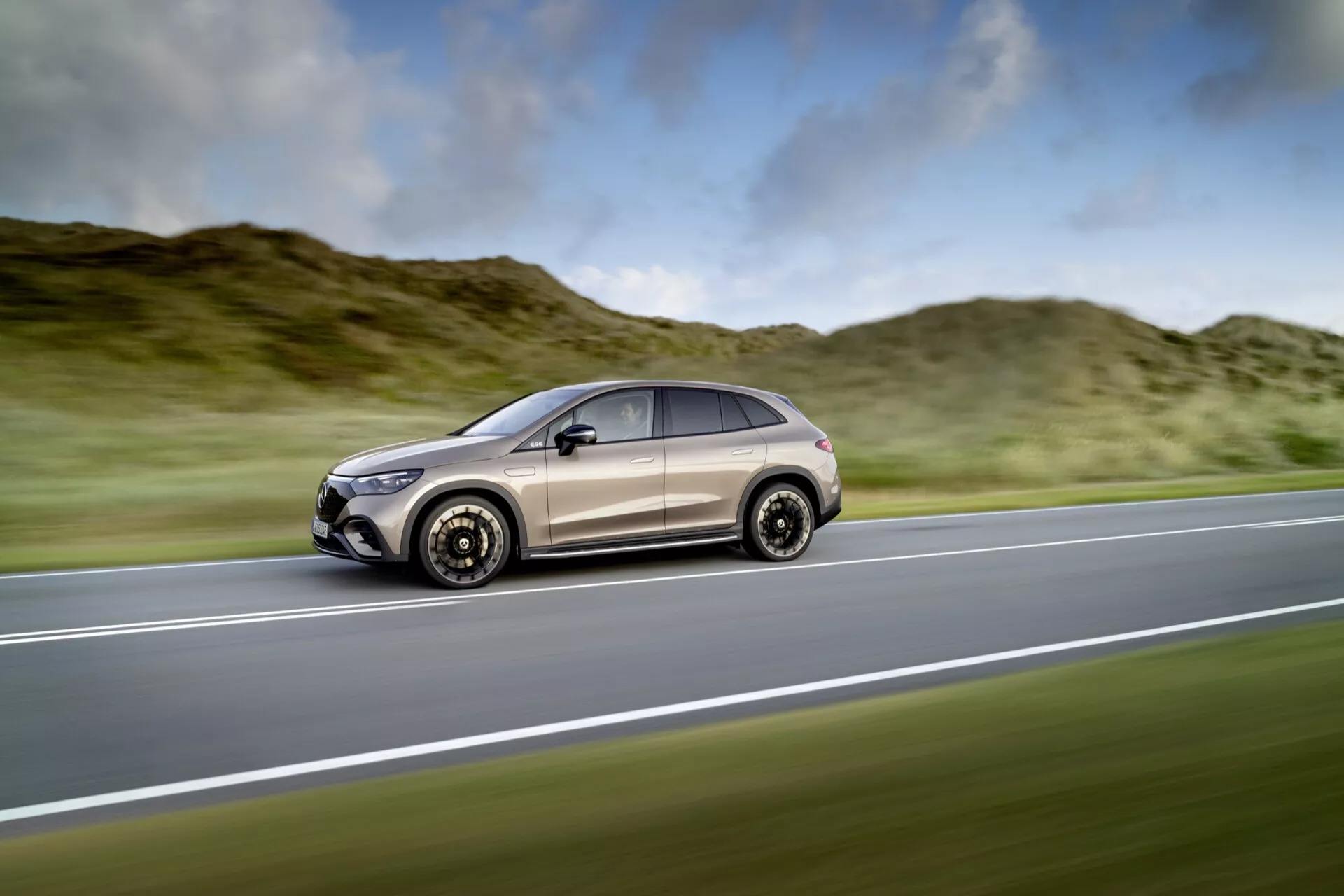 Mercedes-Benz EQE-SUV 2023 v pohybe na diaľnici, predvádzajúce svoj štýlový aerodynamický dizajn, moderné uhlové svetlomety a zliatinové kolesá proti rozostrenému prírodnému pozadiu zdôrazňujúce rýchlosť a ducha dobrodružstva