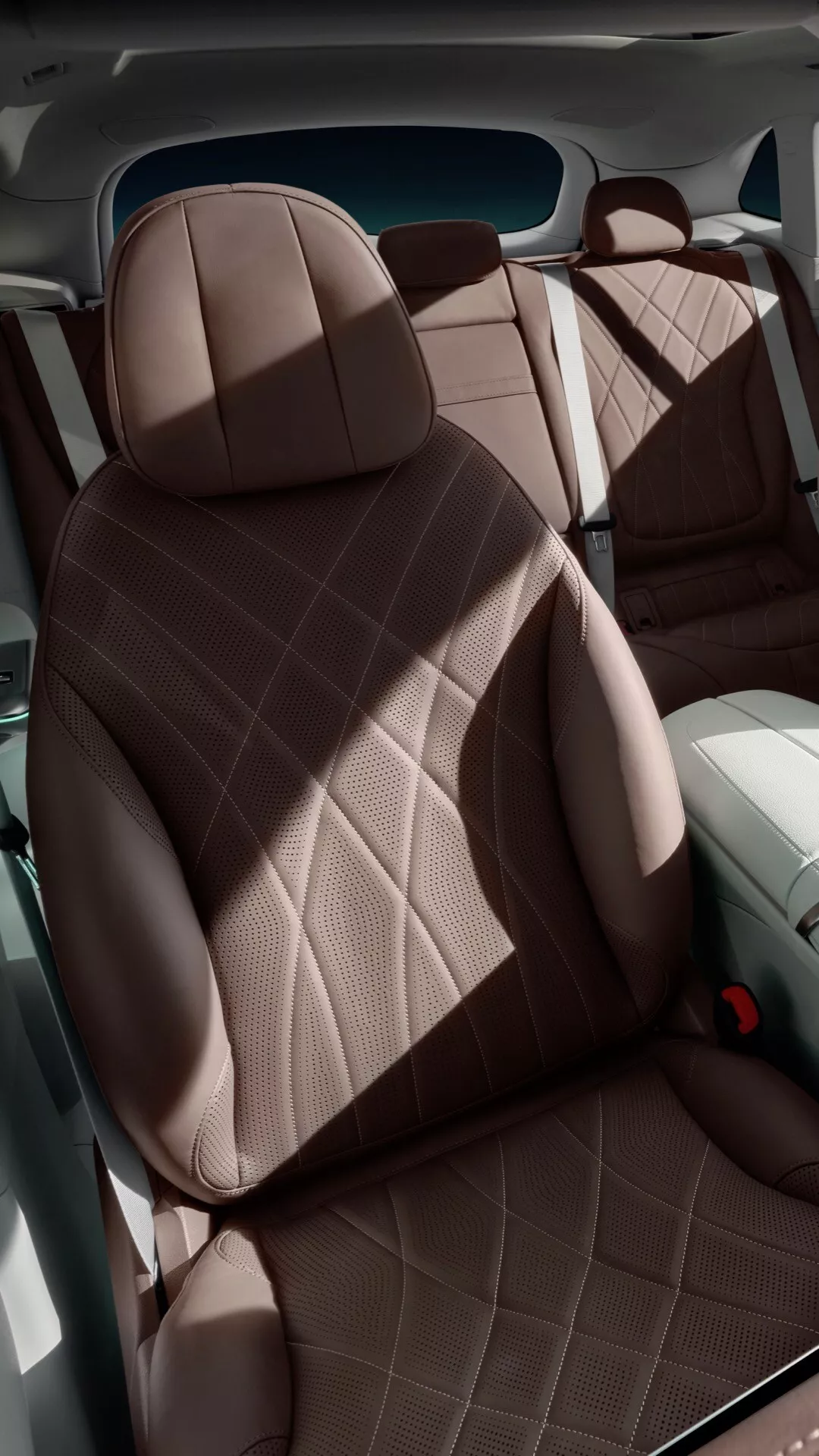 Interiér Mercedes-Benz EQE-SUV 2023 s luxusnými sedadlami z hnedočervenej kože s diamantovým prešívaním, zameraný na ergonomické sedadlo vodiča s jasným výhľadom na prístrojovú dosku a čiastočné zadné sedadlo