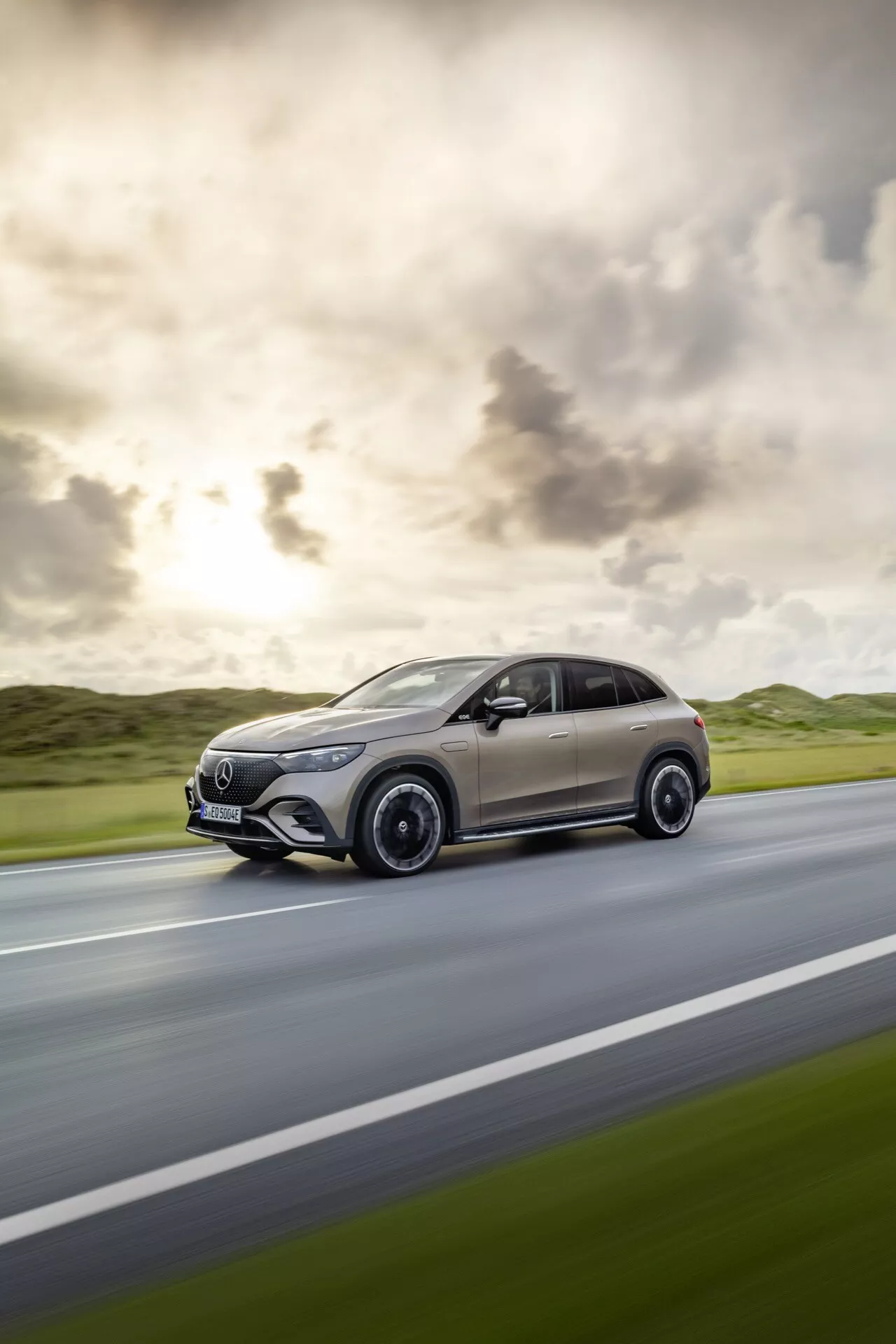 SUV Mercedes-Benz EQE 2023 v pohybe, zobrazujúce jeho dynamický bočný profil s evidentným rozostrením pohybu znázorňujúcim rýchlosť, moderný crossover dizajn so štíhlymi aerodynamickými líniami a luxusnými detailmi v dramatickom osvetlení