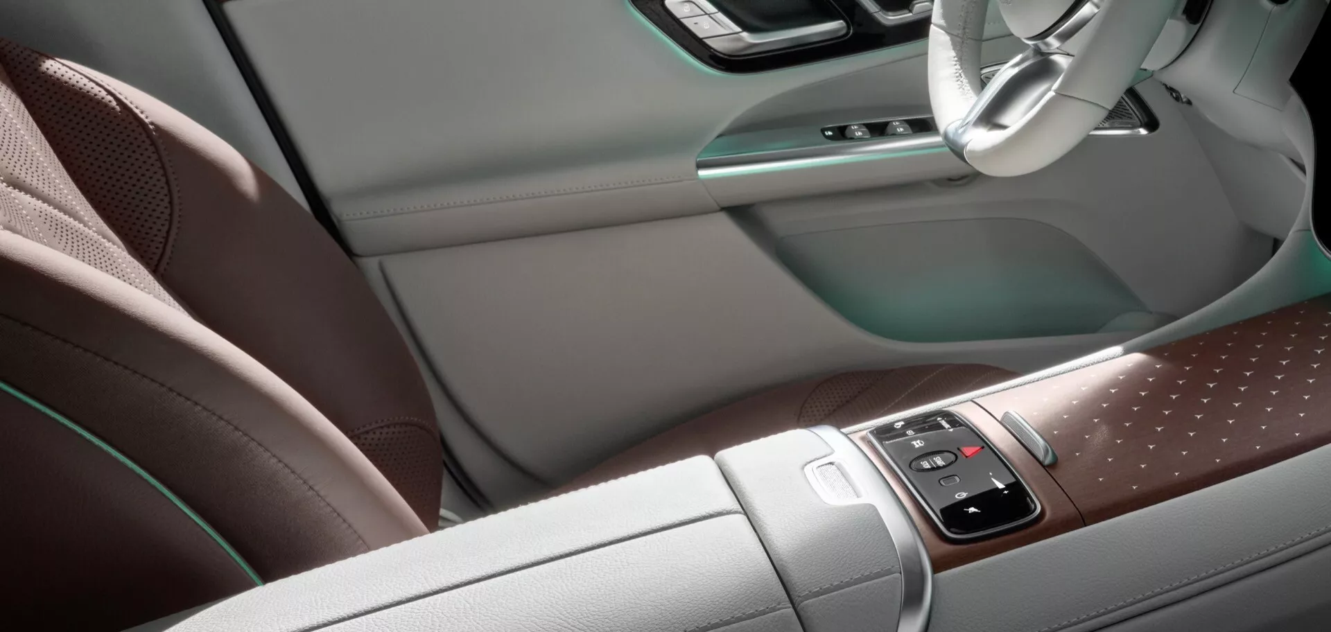 Interiér Mercedes-Benz EQE-SUV 2023 s výhľadom na stredovú konzolu a stranu vodiča, perforované kožené sedadlá, dotykové ovládanie médií a navigácie s drevenými prvkami, tlačidlá klimatizácie a multifunkčný volant pre luxusný a vysoko technologický zážitok z jazdy