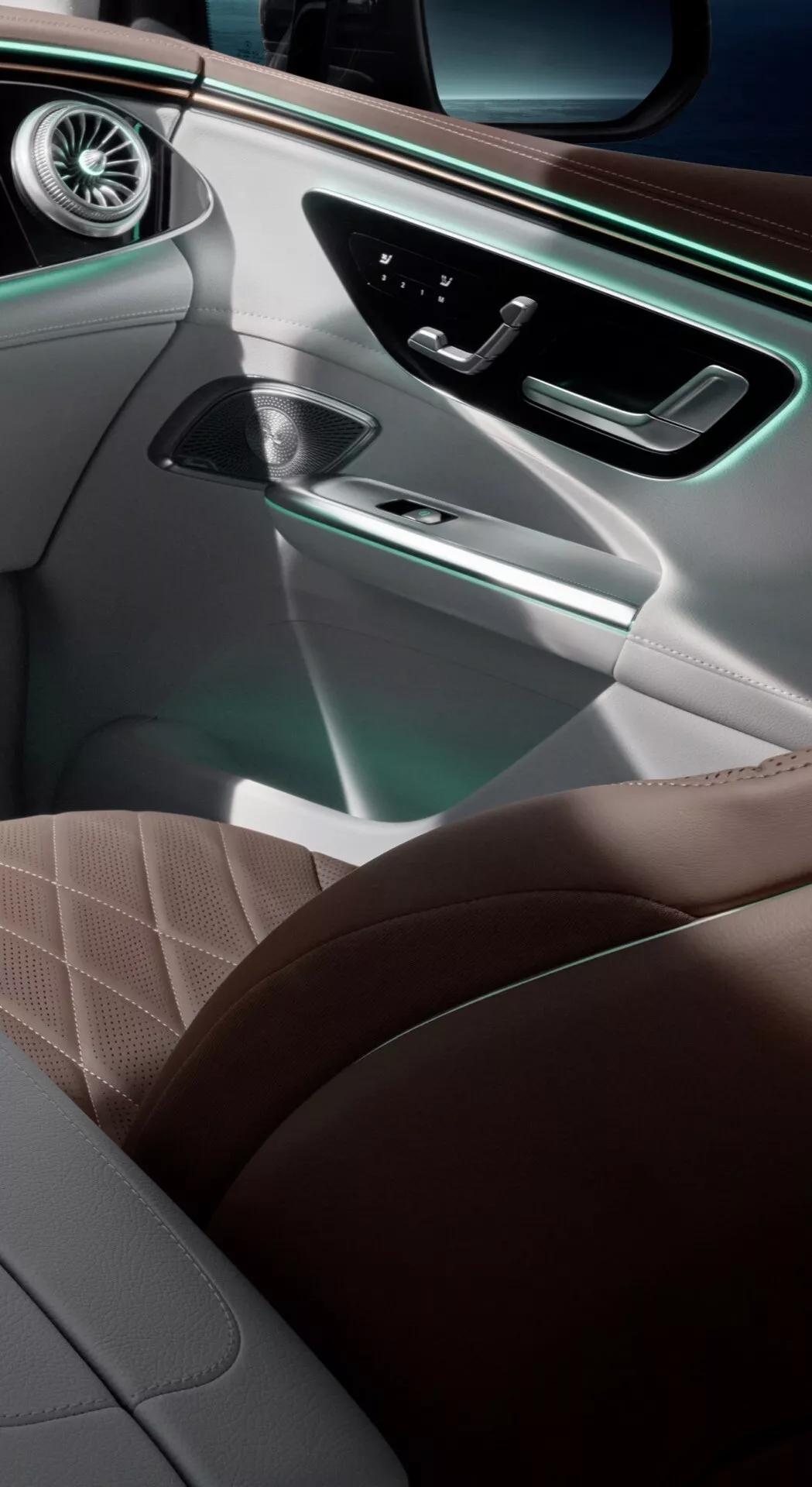 Detailný pohľad na interiér SUV Mercedes-Benz EQE 2023 zobrazujúci dvere a sedadlo spolujazdca s kožou svetlohnedé farby s diamantovým vzorom, drevodekorom, chrómovými prvkami, ambientným osvetlením a pokročilými technologickými funkciami