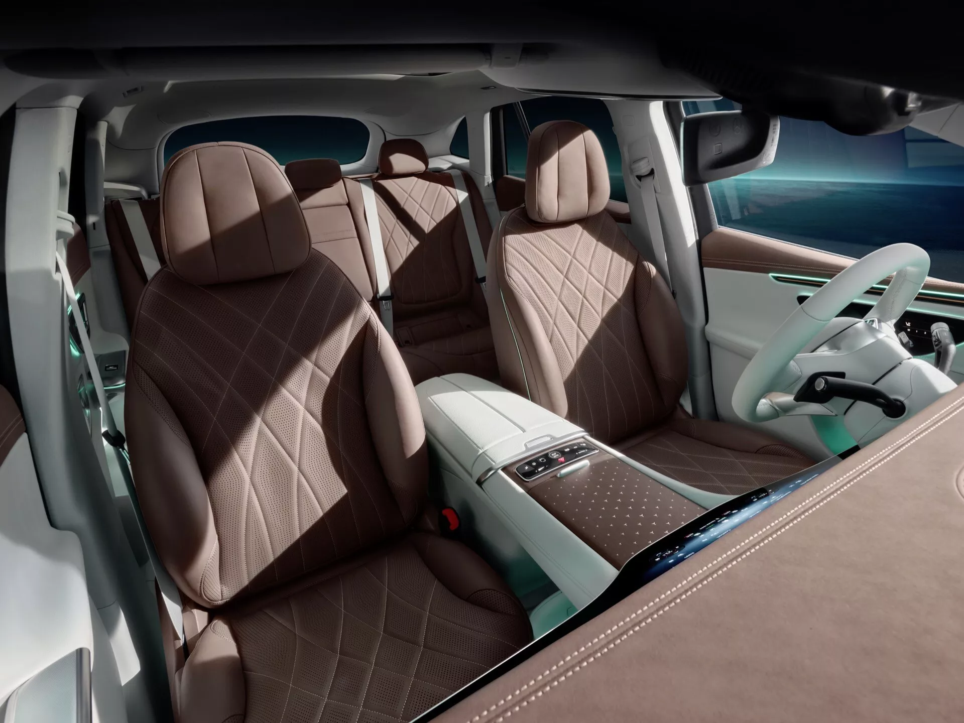 Interiér Mercedes-Benz EQE-SUV 2023 z pohľadu zadných dverí zameraný na luxusné predné sedadlá s hnedým diamantovým prešívaním, pokročilé ovládacie prvky na stredovej konzole a dvojfarebnú palubnú dosku s digitálnymi displejmi a ambientným osvetlením