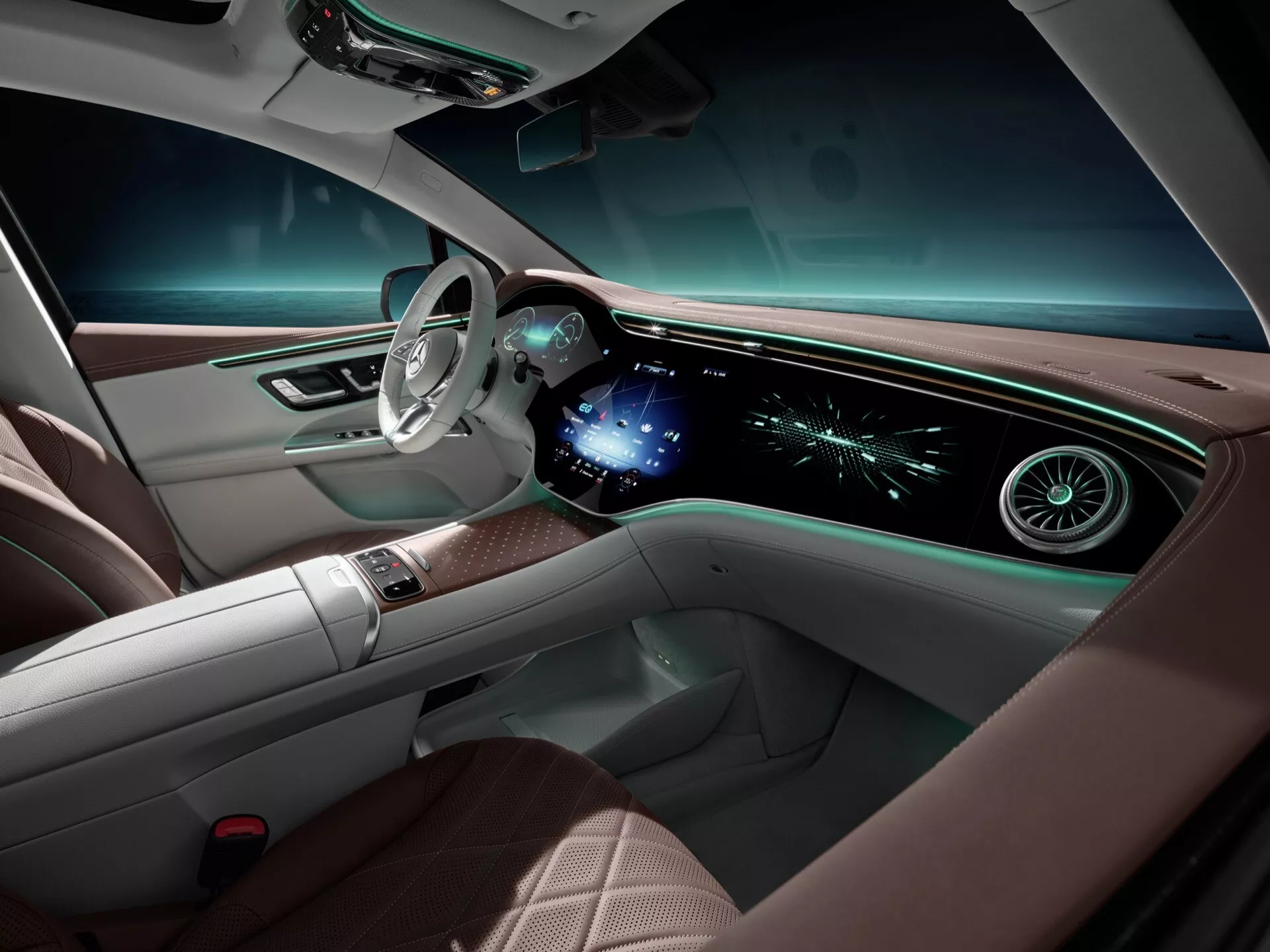 Interiér Mercedes-Benz EQE-SUV 2023 z pohľadu predného spolujazdca, zobrazuje luxusnú palubnú dosku s nepretržitým digitálnym displejom pre navigáciu a informácie o vozidle, ergonomický volant s tlačidlami ovládania a materiály vysokej kvality s ambientným osvetlením