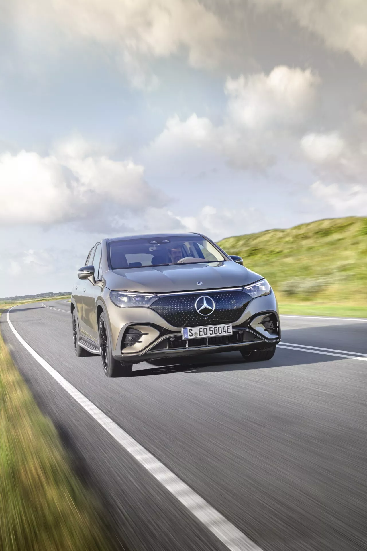 Mercedes-Benz EQE SUV z roku 2023 idúce po vidieckej ceste pod jasným nebom, ktoré zdôrazňuje jeho dynamický dizajn a luxusné prvky z uhla predných troch štvrtín