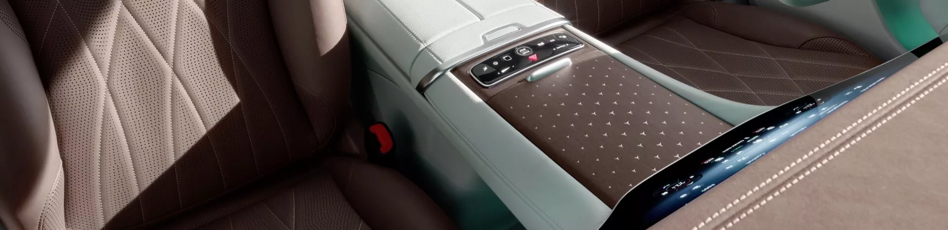 Interiér Mercedes-Benz EQE-SUV 2023 ukazujúci elegantnú stredovú konzolu, sedadlá vysokej kvality s béžovým diamantovým šitím, potenciálne miesto pre bezdrôtové nabíjanie, chrómovú lištu s detailným šitím, ambientné osvetlenie a konektivitné porty, zobrazenie z boku a mierne zdola.