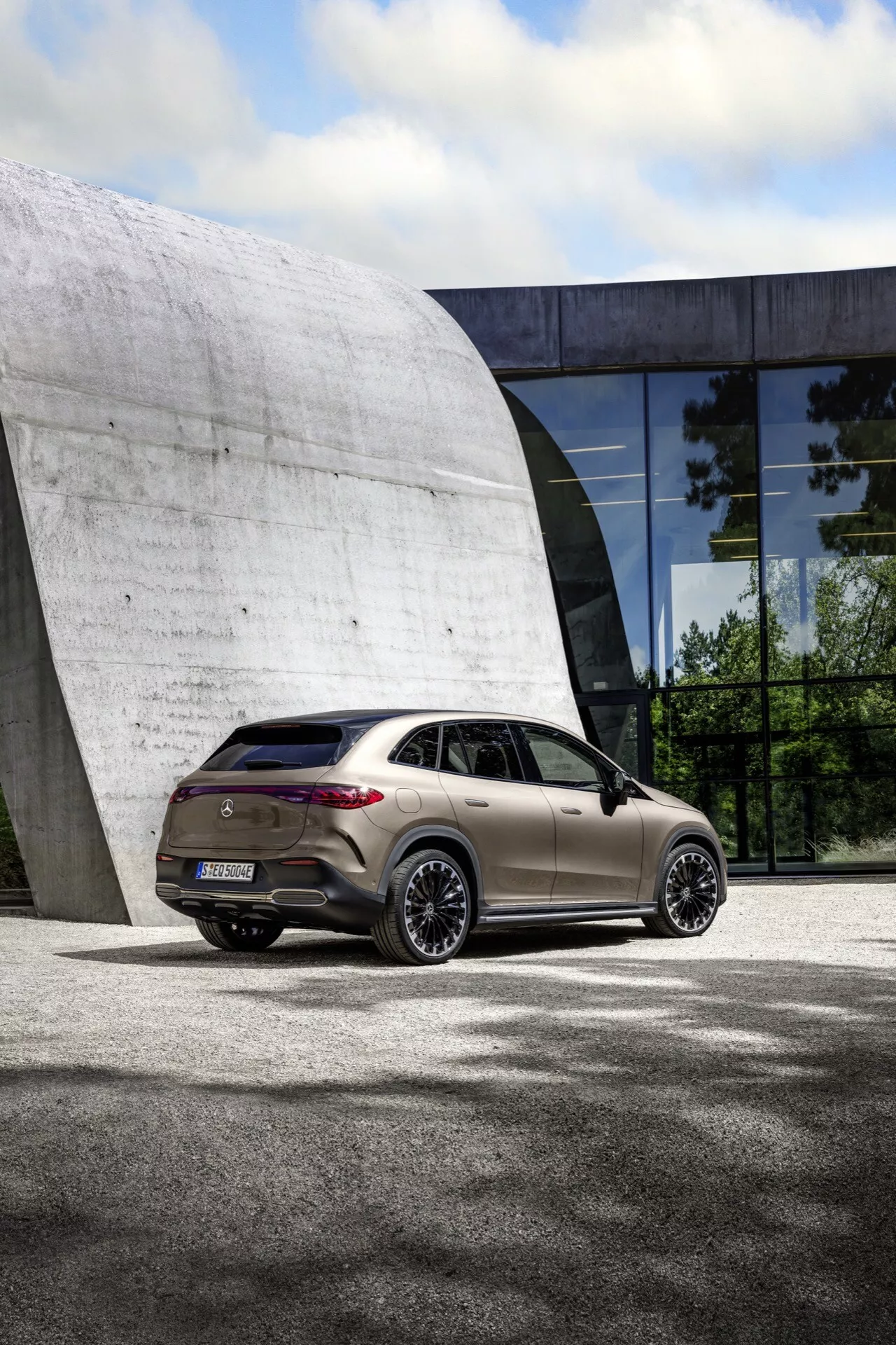 Mercedes-Benz EQE SUV 2023 zaparkované na chodníku s budúcnostou budovou na pozadí, zdôrazňujúce elegantný dizajn, zliatinové kolesá, LED zadné svetlá a aerodynamické prvky z pohľadu z troch štvrtín zozadu