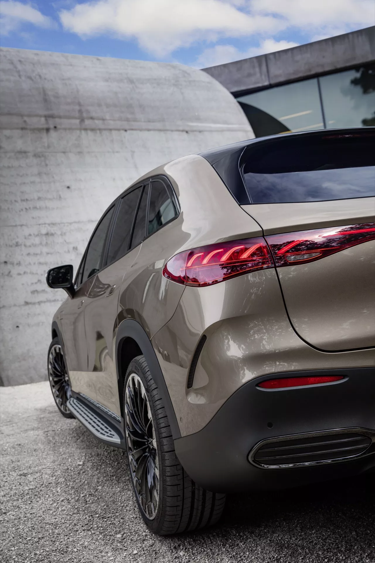 Detailný zadný trojštvrťový pohľad na Mercedes-Benz EQE-SUV 2023, zobrazujúci LED zadné svetlá, integrované parkovacie senzory, dvojitý výfuk, metalický lak a hliníkové disky s viacerými ramenami na pozadí mestské architektúry pod zamračenou oblohou