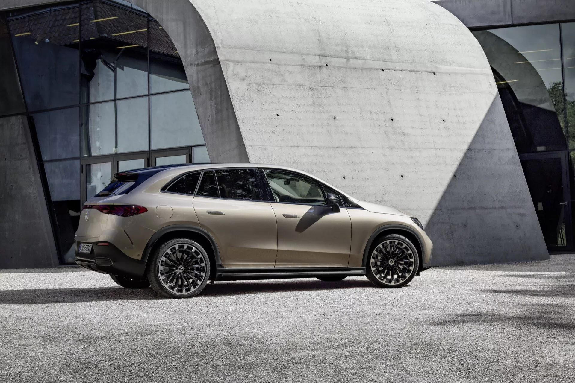 Model Mercedes-Benz EQE SUV 2023 predvádzaný v matnej zlatej béžovej farbe, zachytený z bočného profilového uhla ukazujúceho bok a čiastočný zadný pohľad, s výrazným dizajnom disku a štýlovým dizajnom coupé SUV.