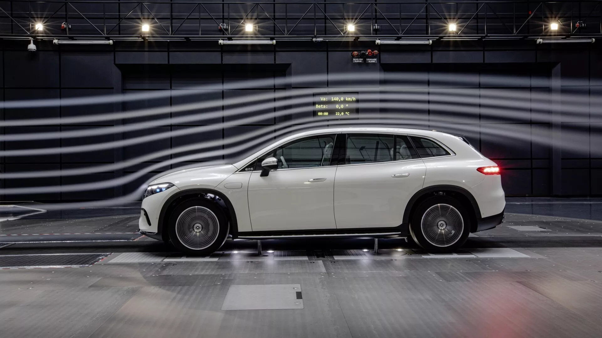 Bočný profilový pohľad na Mercedes EQS SUV 2022 na zážitkovej trati, zdôrazňujúci jeho elegantný dizajn, zliatinové kolesá a reflexný, dobre udržiavaný exteriér. Moderný luxusný crossover SUV má strešnú líniu mierne klesajúcu vzadu, čo naznačuje športovú estetiku kombinovanú s praktickosťou SUV. Fotografia zachytáva celkovú dĺžku vozidla s rozmazanými čiarami v pozadí simulujúcimi vysokú rýchlosť, zdôrazňujúc dizajn a predpokladané výkonné vlastnosti vozidla v kontrolovanom, monochromatickom prostredí.
