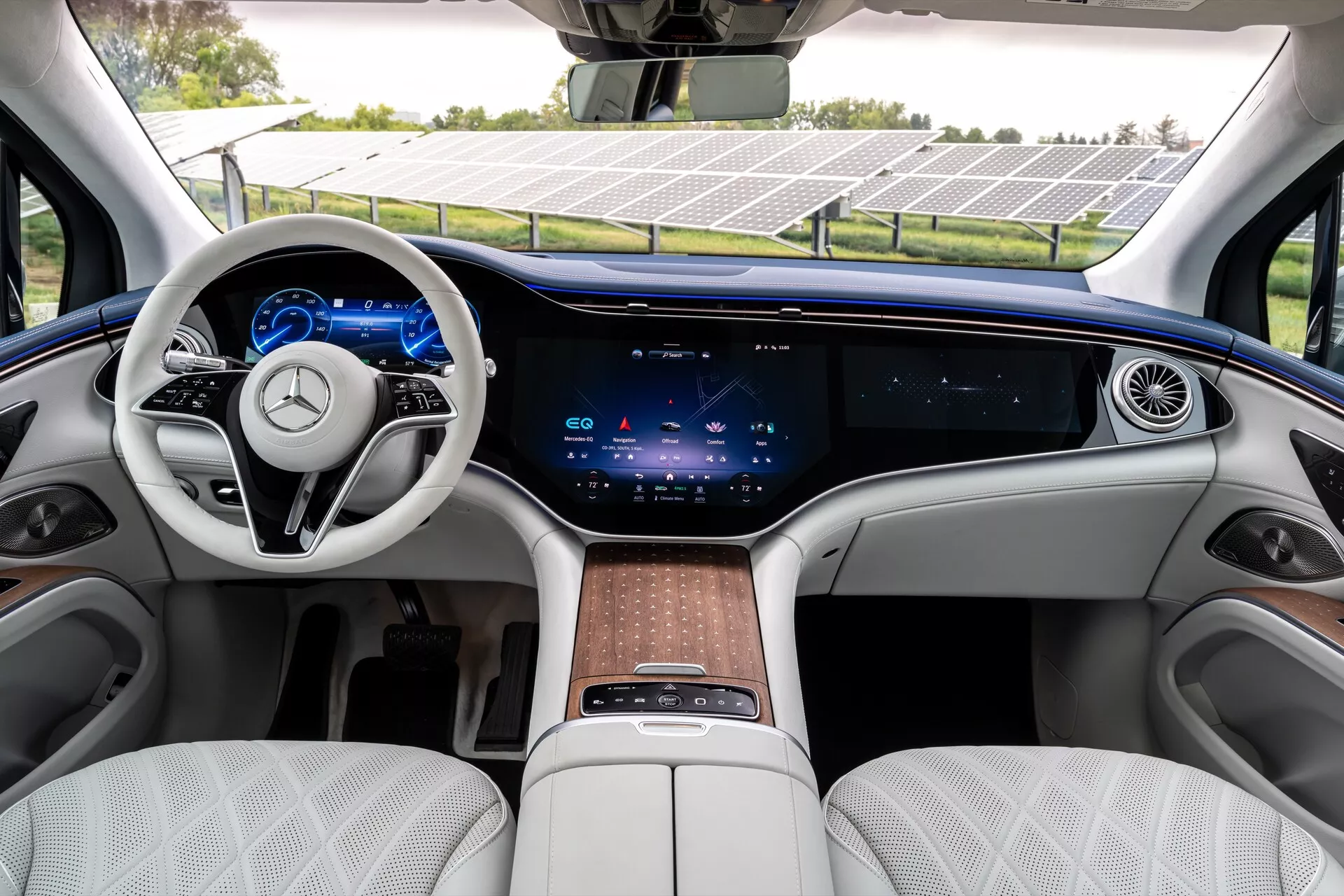 Interiér Mercedesu EQS-SUV 2022, ktorý predvádza luxusný predný rad s volantom s dvoma lúčmi, integrovanými dotykovými ovládacími prvkami, plne digitálnym prístrojovým panelom, rozsiahlou dotykovou obrazovkou uprostred palubnej dosky, minimálnymi fyzickými ovládacími prvkami pre klimatizáciu, kontinuálnym ventilačným otvorom, bielymi prešívanými koženými sedadlami, drevenými obkladmi a centrálnou konzolou s dotykovou podložkou a úložným priestorom.