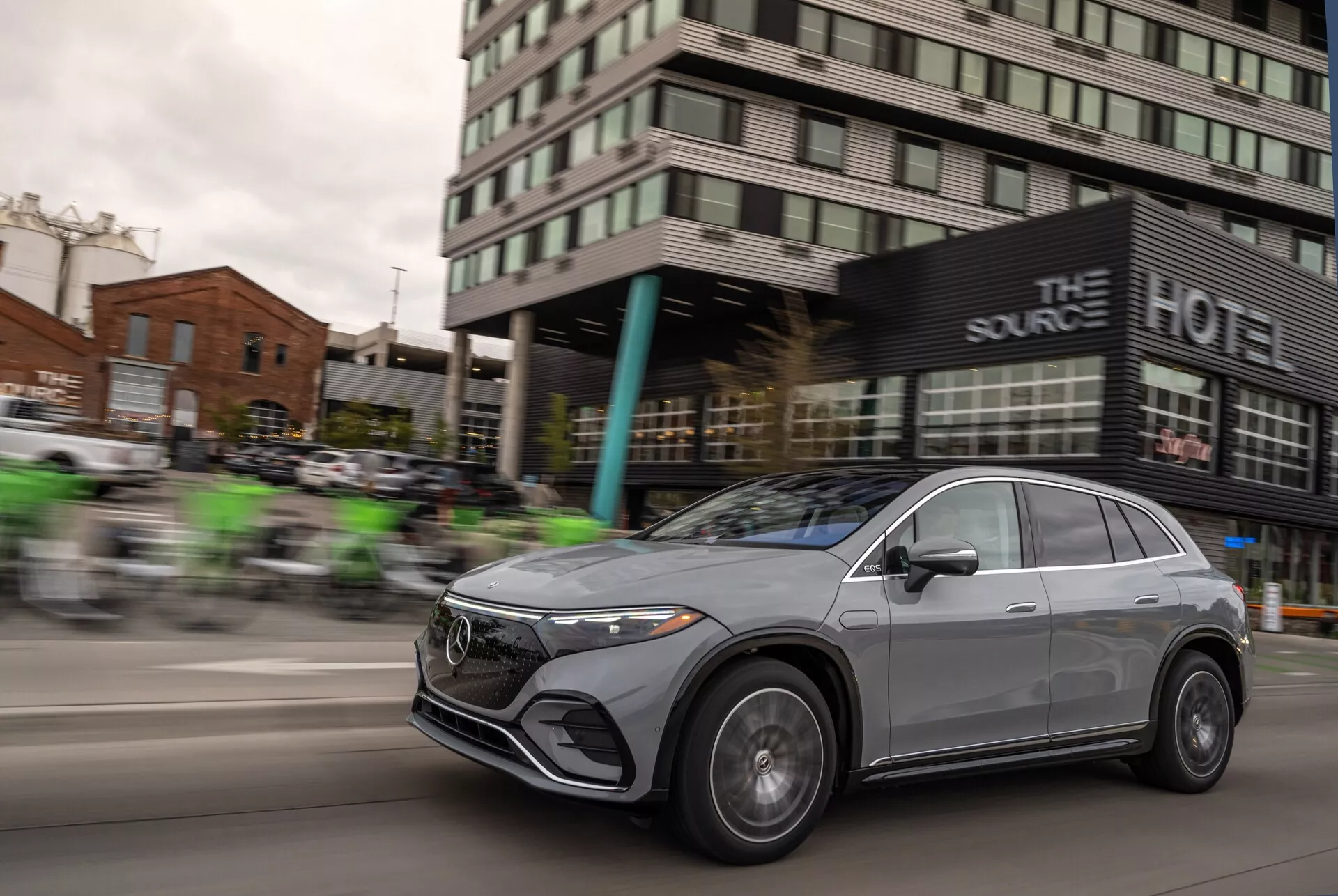 Dynamický záber na Mercedes EQS-SUV 2022 v pohybe, s efektom rozmazania, ktorý zvýrazňuje rýchlosť vozidla. Výrazné sú predná mriežka, LED svetlomety, zliatinové kolesá a aerodynamický dizajn kapoty a strešnej línie, čo podčiarkuje sofistikované a luxusné prvky vozidla. Kovový povrch a crossoverový štýl s elegantnými bezrámovými oknami a aerodynamicky tvarovanými zrkadlami pridávajú moderný a špičkový vzhľad.
