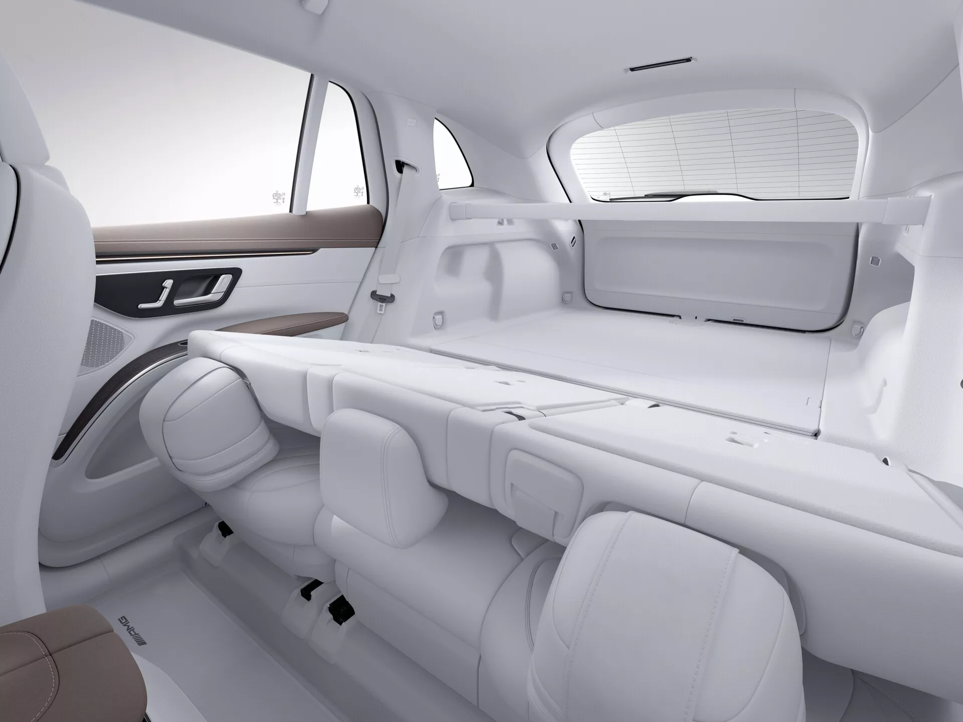 Interiér Mercedes EQS SUV 2022 so zameraním na zadné sedadlá a časť kufra. Obraz je urobený z šikmého uhla, mierne nad výškou sedadiel, zvýrazňuje usporiadanie sedadiel a priestor. Monochromatický biely tón zdôrazňuje čistý, moderný dizajn. Zadné sedadlá sú v lavicovej konfigurácii s troma nastaviteľnými opierkami hlavy a individuálnymi bezpečnostnými pásmi. Bočné dvere majú drevený obklad a integrované ovládacie prvky, pravdepodobne pre okná alebo iné elektronické funkcie. Zadné okno je vybavené slnečnou clonou a viditeľná je aj plochá polica, čo zdôrazňuje komfort cestujúcich a luxusné prvky.