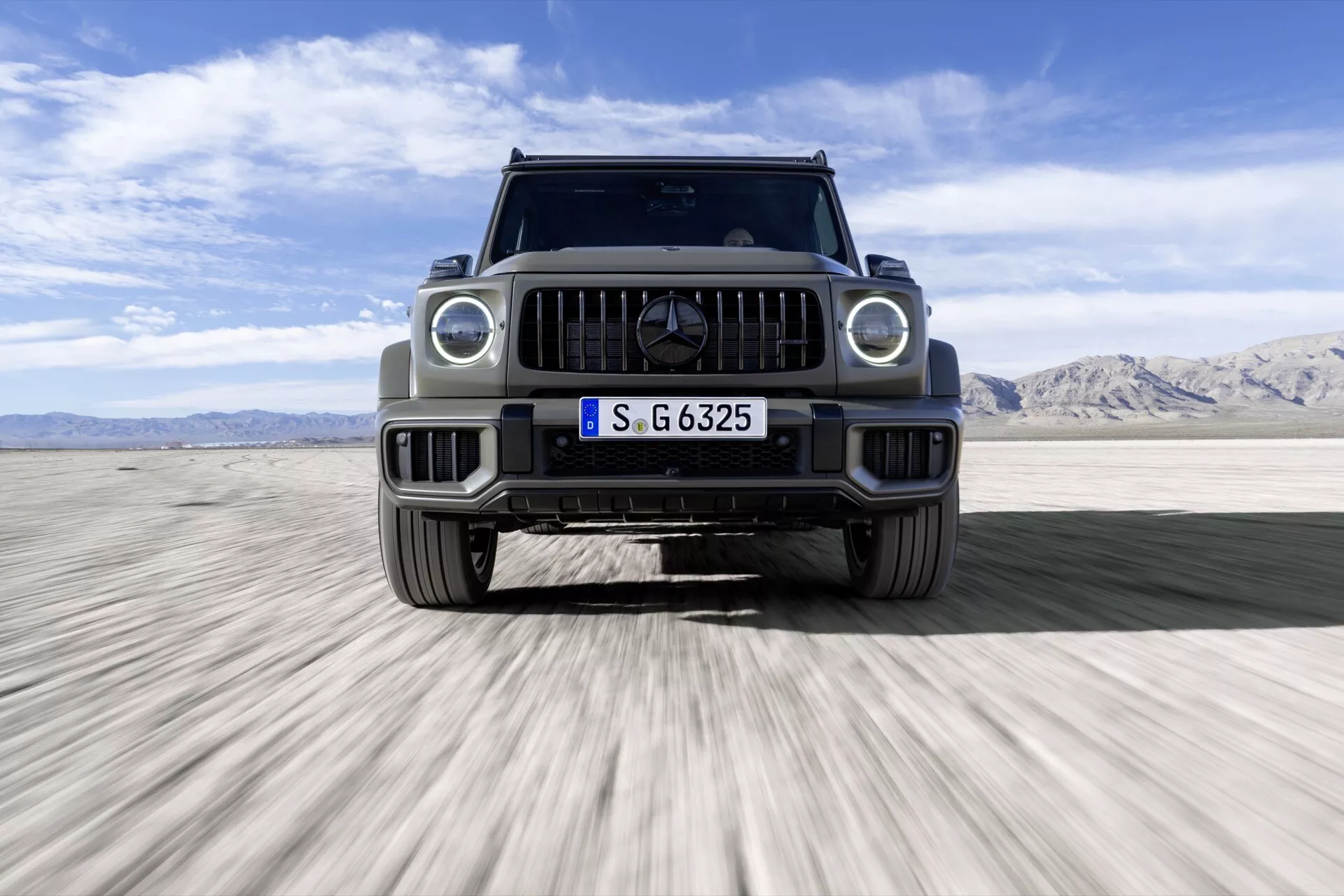 Luxusné SUV Mercedes-Benz triedy G (G 465) pre rok 2024, pohľad spredu na púšti, predvádzajúce LED svetlomety, charakteristickú mriežku s emblémom a schopnosti pre terénne jazdenie.