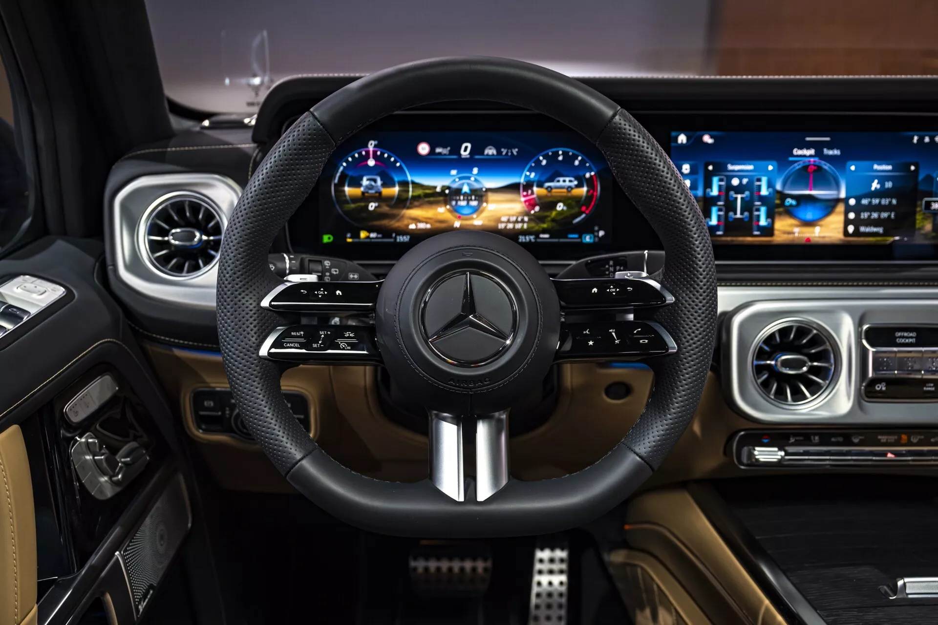 Interiér Mercedes-Benz triedy G (G-Klasse) pre rok 2024 z pohľadu vodiča, obsahuje kožou obalený volant s emblémom Mercedes a kovovými akcentmi, digitálny prístrojový panel a širokouhlý panel infotainment