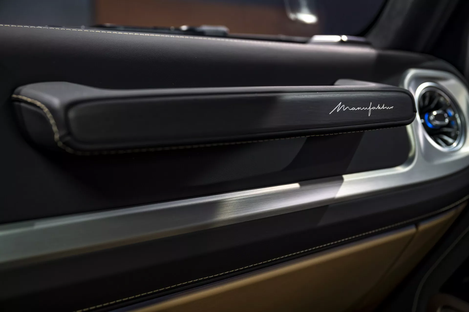 Detailný pohľad na časť dverového panelu Maserati zameraný na elegantnú, modernú kľučku dverí s kovovým lemom a možným ovládacím tlačidlom, zvýrazňujúci luxusné detaily interiéru.