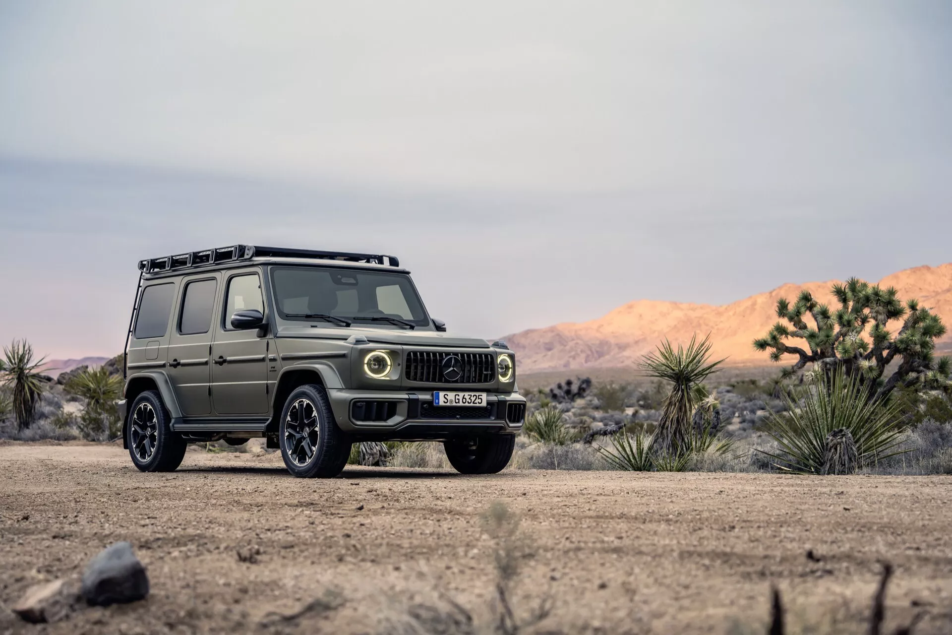 SUV Mercedes-Benz G-Klasse 2024 v prírodnom a náročnom prostredí, zobrazujúci pohľad z predného trojštvrtečného uhla s detailným zobrazením mriežky, svetlometov a kolies vhodných pre jazdu v teréne na poľnej ceste