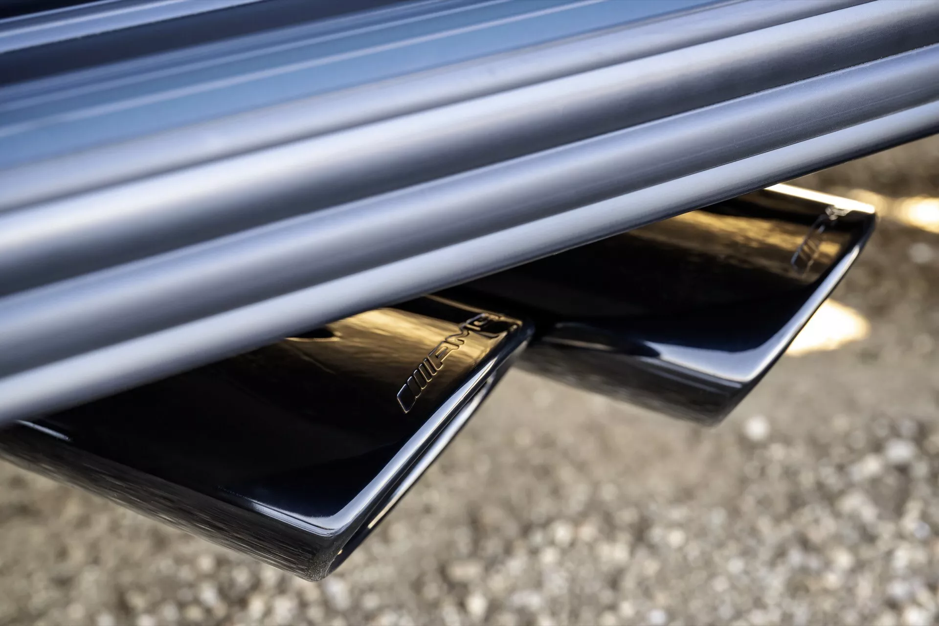 Detailný pohľad na dvojité výfukové koncovky Mercedes-Benz triedy G (G 465) ročník 2024 s chrómovým povrchom, integrované do zadného nárazníka pre štýlový vzhľad, zdôrazňujúce výkon a estetickú kvalitu vozidla.