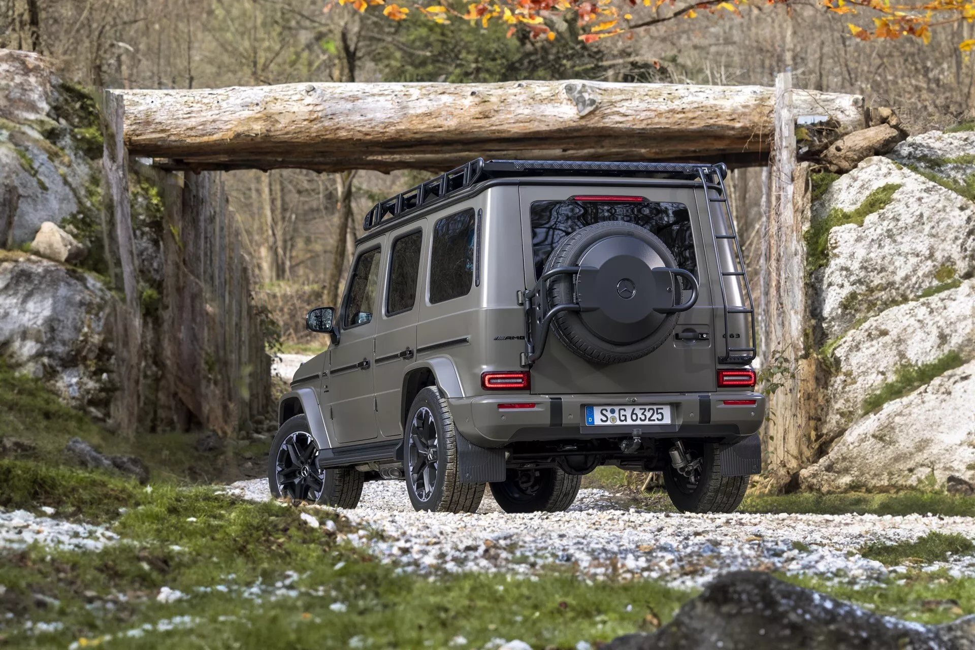 Zadný uhlový pohľad na SUV Mercedes-Benz G-Klasse 465 z roku 2024, zdôrazňujúci výšku a svetlú výšku na skalnatom teréne, vybavené rezervným kolieskom, prijímačom ťažného zariadenia a predvádzajúci jeho off-road schopnosti