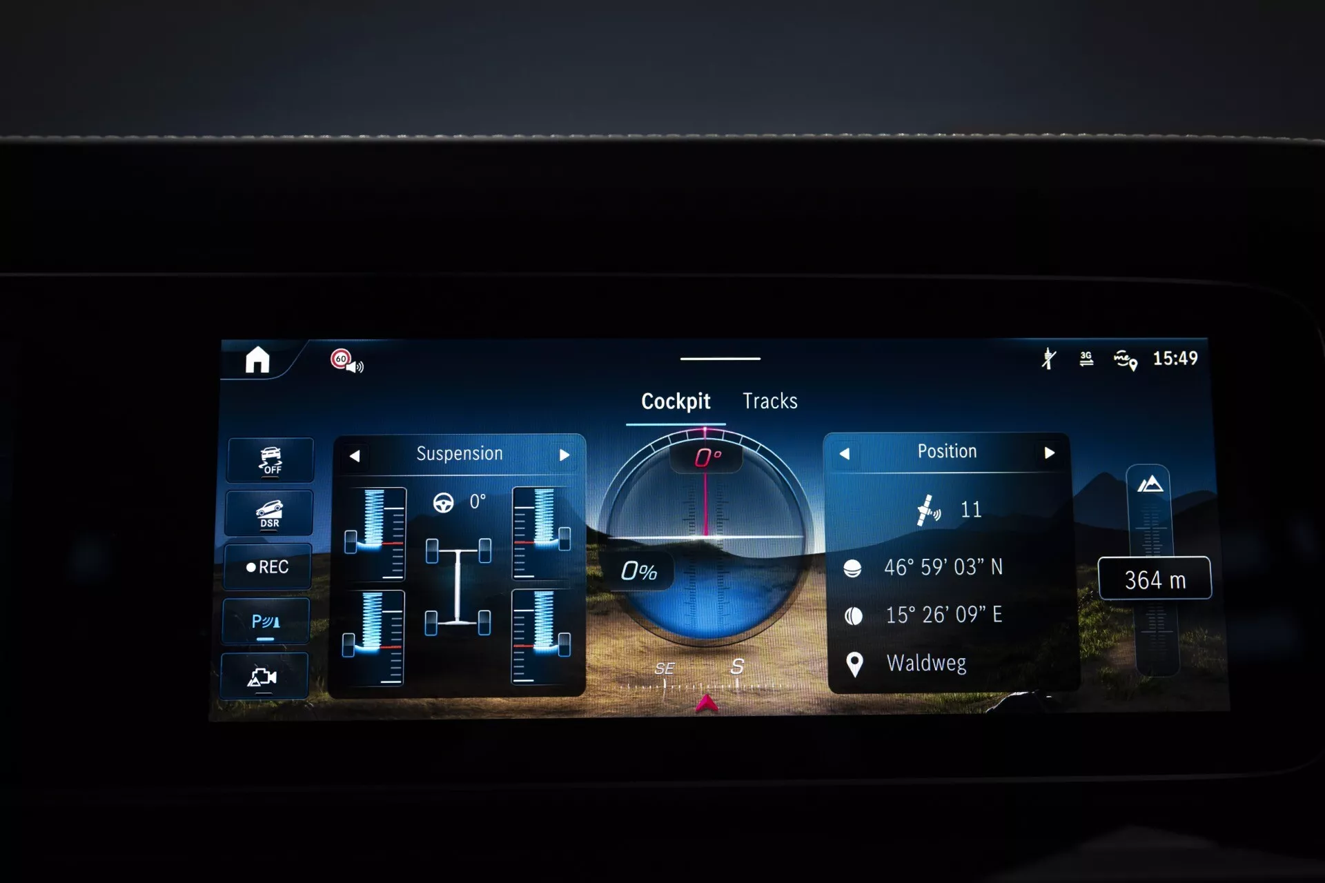 Displej informačno-zábavného systému Mercedes-Benz G-Klasse 2024 ukazujúci nastavenia zavesenia, GPS súradnice, prispôsobiteľné informácie o kokpite a funkciu záznamu jazdných tratí, so zameraním na pokročilú technológiu vozidla