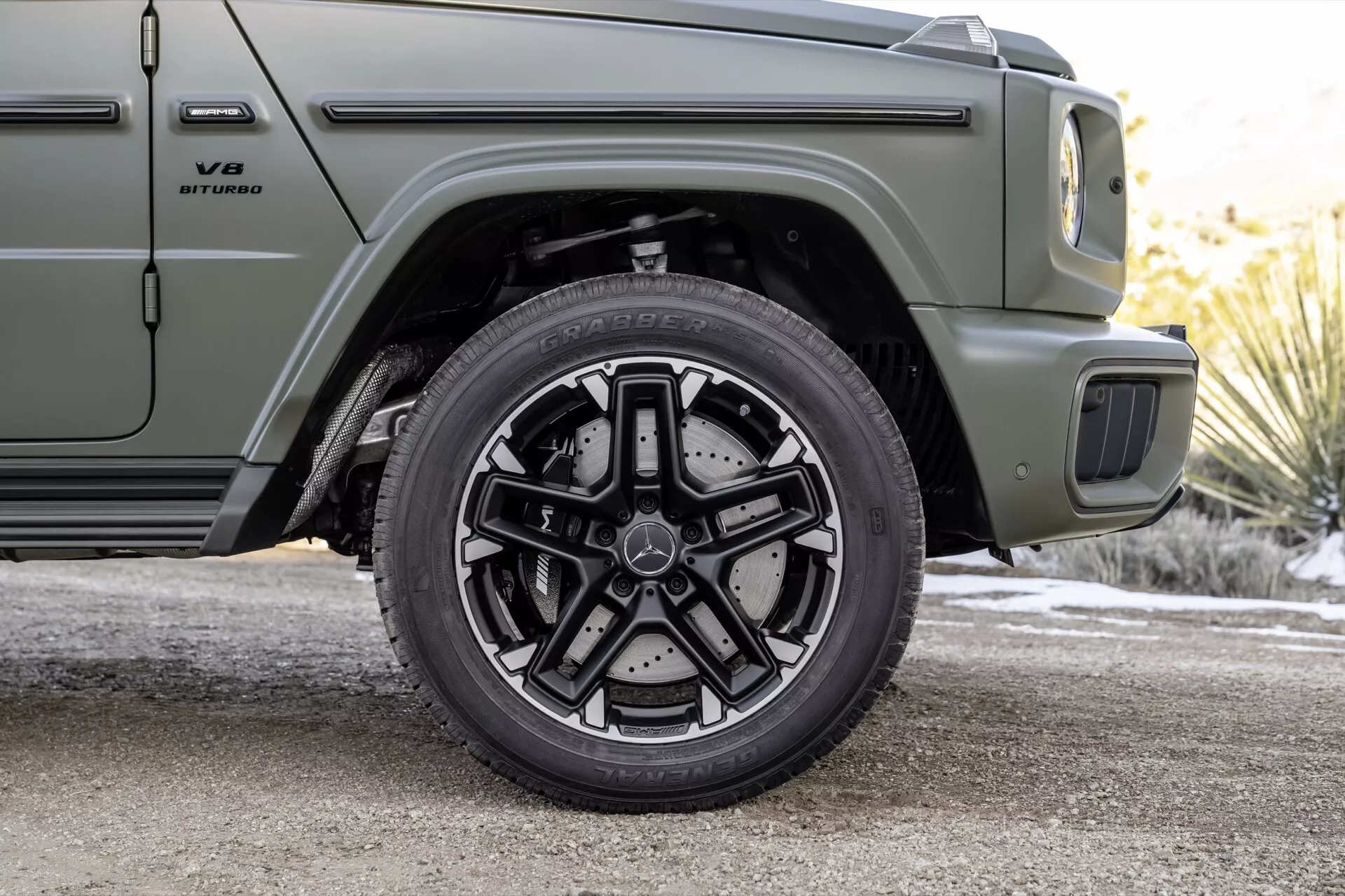 Detailný pohľad na predné pravé koleso a časť bočného profilu Mercedes-Benz G-Klasse 2024, ukazujúci vysokovýkonný brzdový systém a dizajn zliatinového kolesa s viacerými lúčmi, v matnej olivovej zeleni