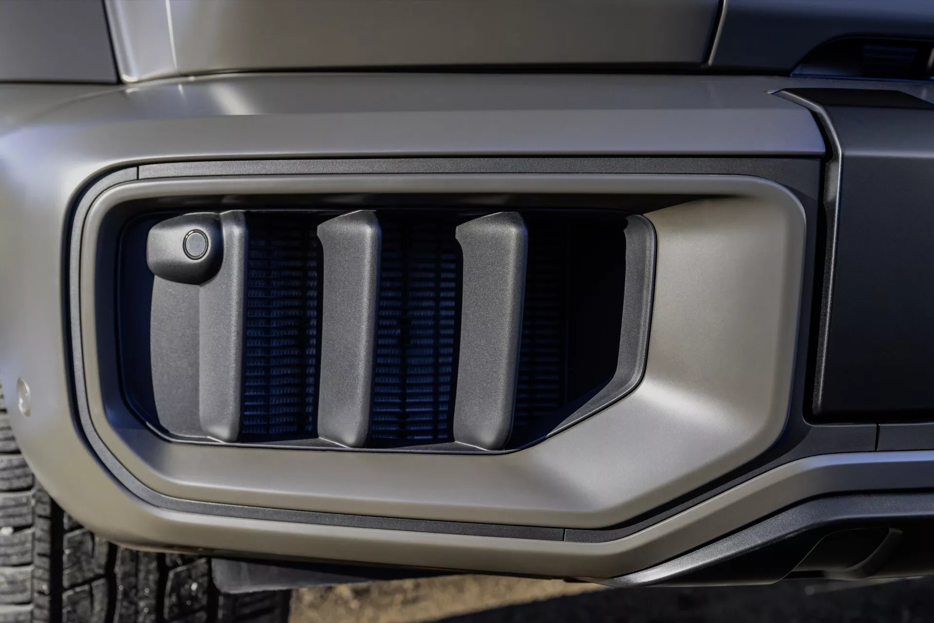 Detailný záber na predný nárazník Mercedes-Benz G-Klasse 2024 s mriežkou sacieho otvoru s integrovaným senzorom, ktorý zdôrazňuje pokročilú technológiu a modernú dizajnovú estetiku.