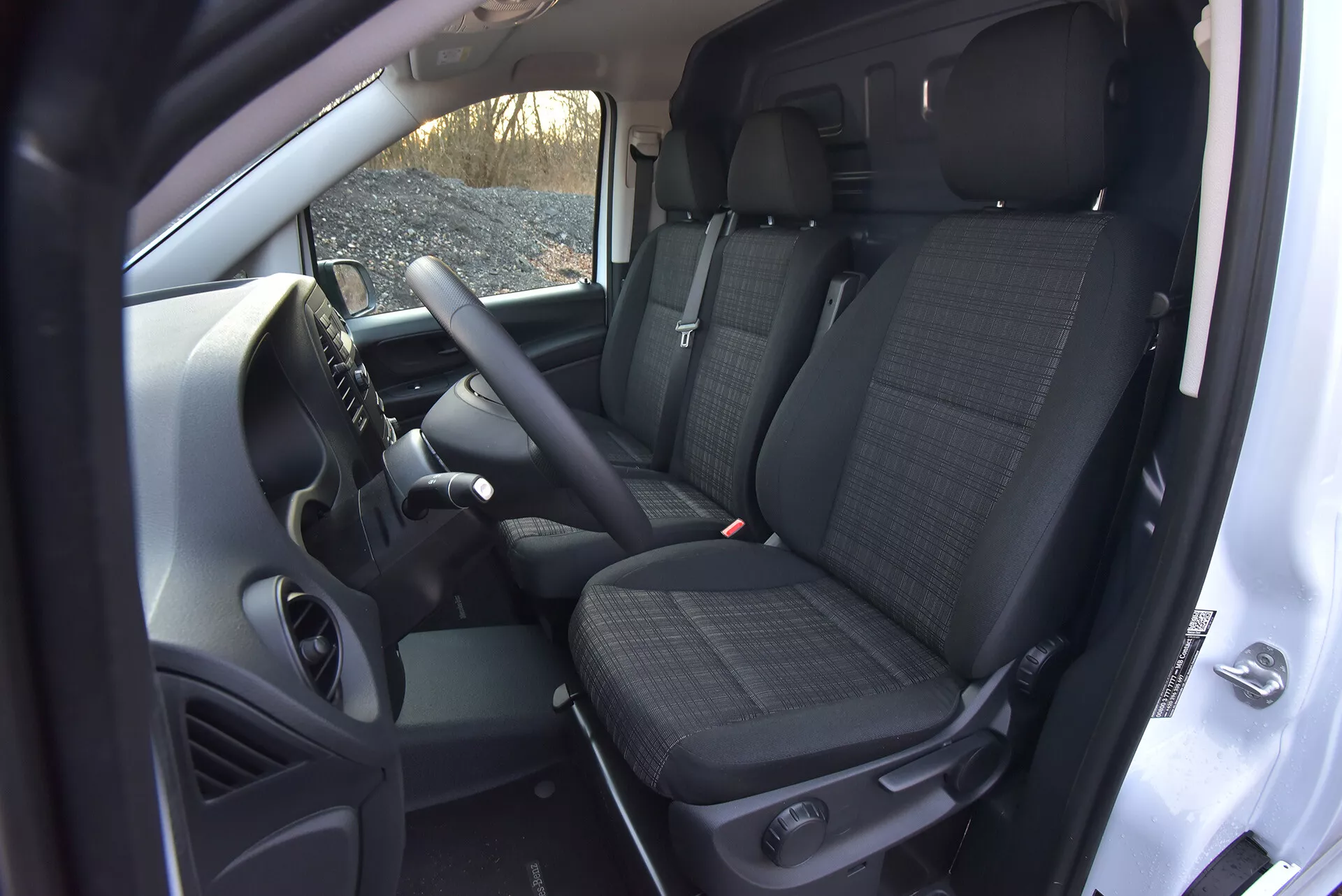 Interiérový pohľad na Mercedes-Benz Vito 2014 (Vito-Tourer) ukazujúci oblasť vodiča a spolujazdca s technologickými prvkami ako ovládacie prvky na volante, centrálna konzola možno obsahujúca systém infotainment, predné sedadlá s vzorovanou látkou s opierkami hlavy, a pohľad na zadné sedadlá, všetko z vysokej uhlové perspektívy zdôrazňujúcej priestrannosť kabíny a prvky manuálnej prevodovky.