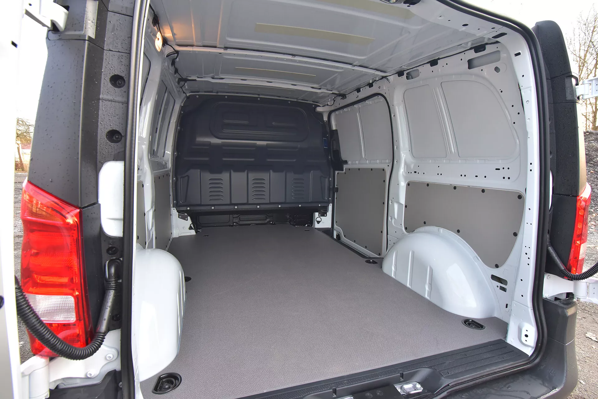 Zadný nákladový priestor obchodného dodávky Mercedes-Benz Vito Tourer 2014 s otvorenými dverami, ktorý ukazuje plochú odolnú podlahu a holý kovový interiér pre ľahkú úpravu, zobrazený z mierne šikmého zadného vonkajšieho uhla