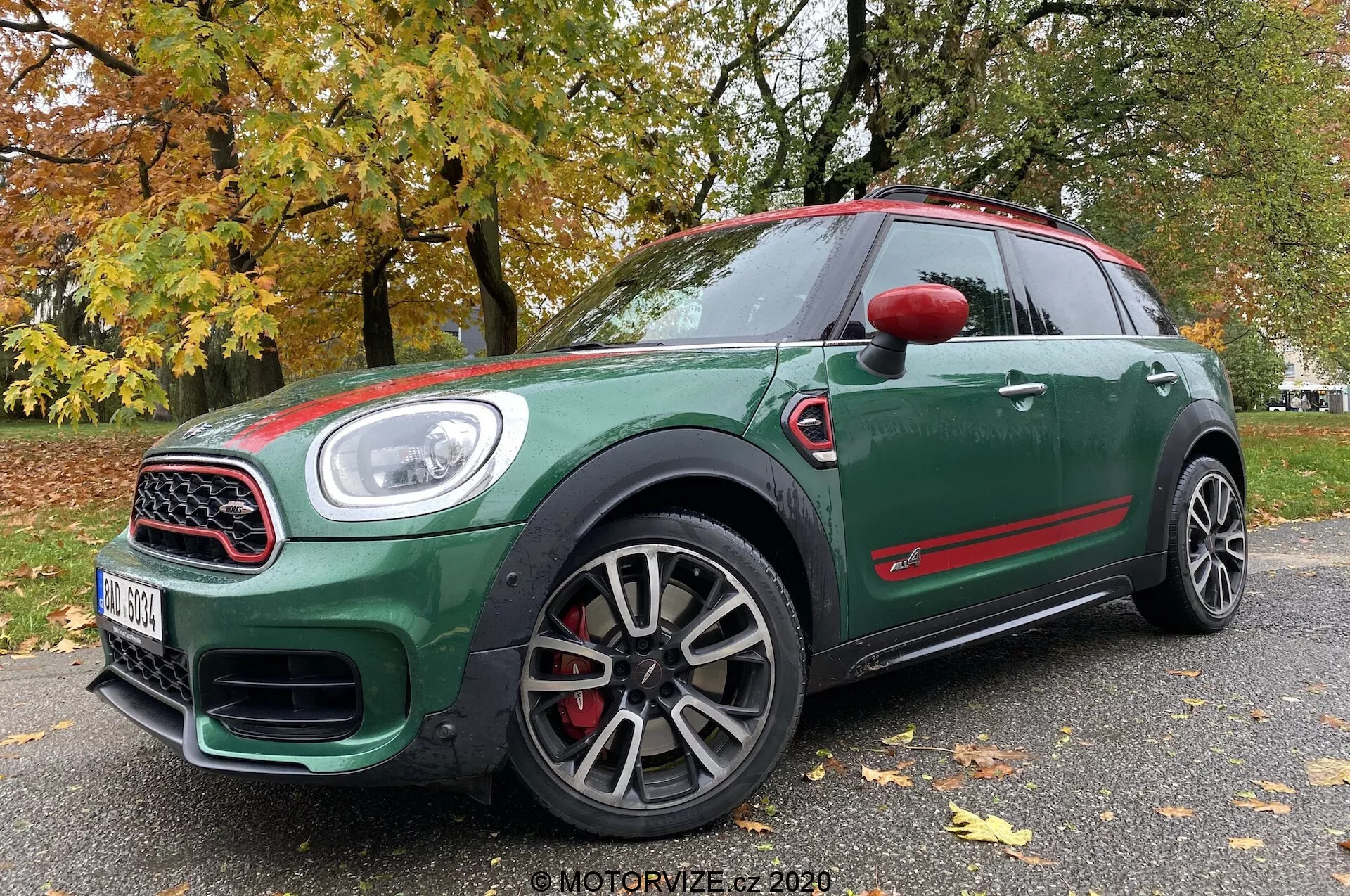 Pohľad z nízkeho predného trojštvrťového uhla na Mini Countryman John Cooper Works 2020, ktorý zobrazuje jeho tmavozelený exteriér s červenými akcentmi, športovými viacramennými kolesami, mriežkou s chrómovým rámom, veľkými vstupmi vzduchu, LED svetlometmi a červenými brzdovými strmeňmi.