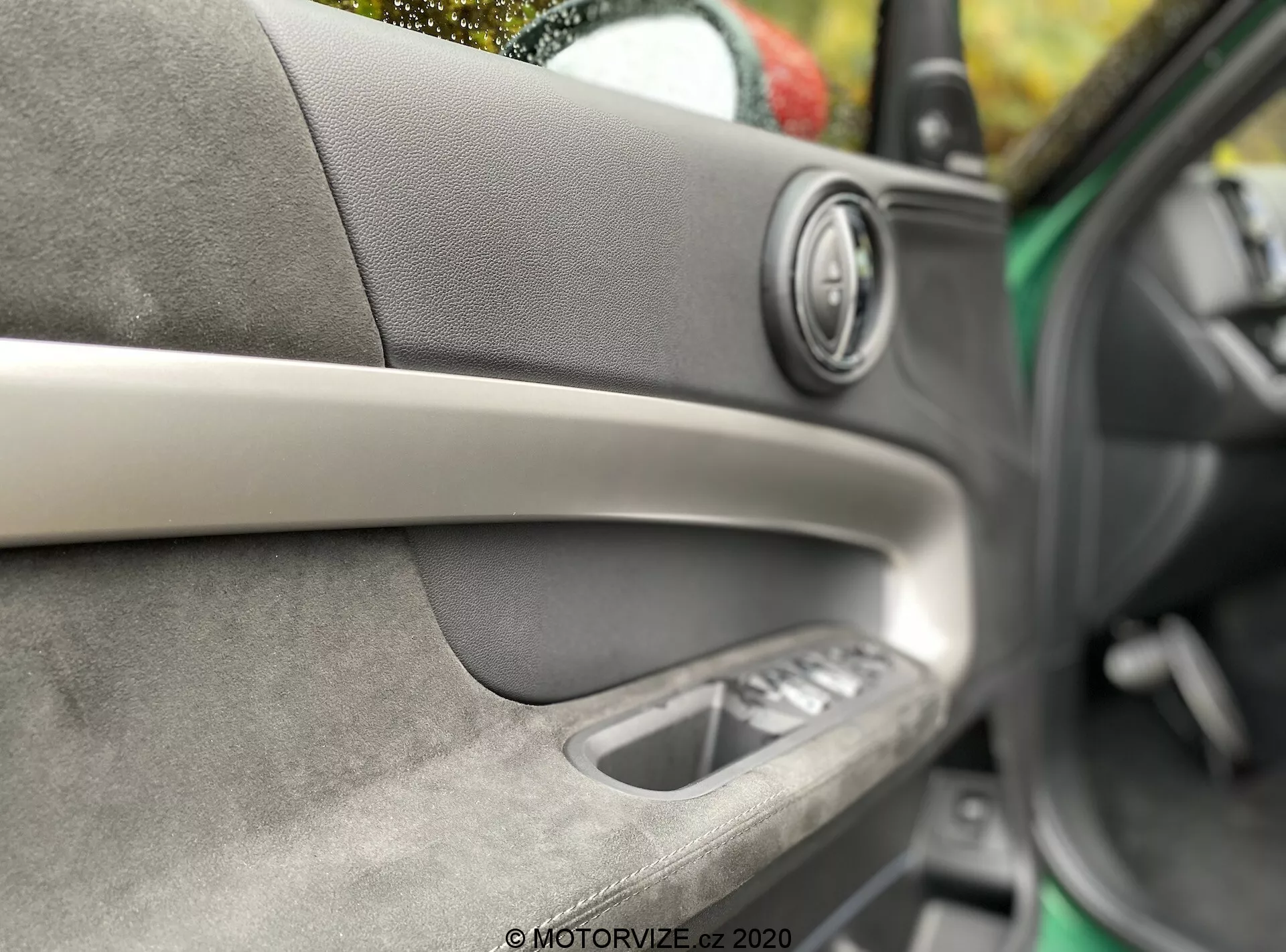 Detailný záber interiéru dverí auta Mini Countryman John Cooper Works 2020. Zamerané na prémiový audio reproduktor s kovovým krúžkom, diagonálny dekoratívny pás, mäkký materiál s viditeľným šitím, vnútornú kľučku dverí a ovládanie okien. Malá hĺbka ostrosti zdôrazňujúca remeselné spracovanie a komfort interiéru.
